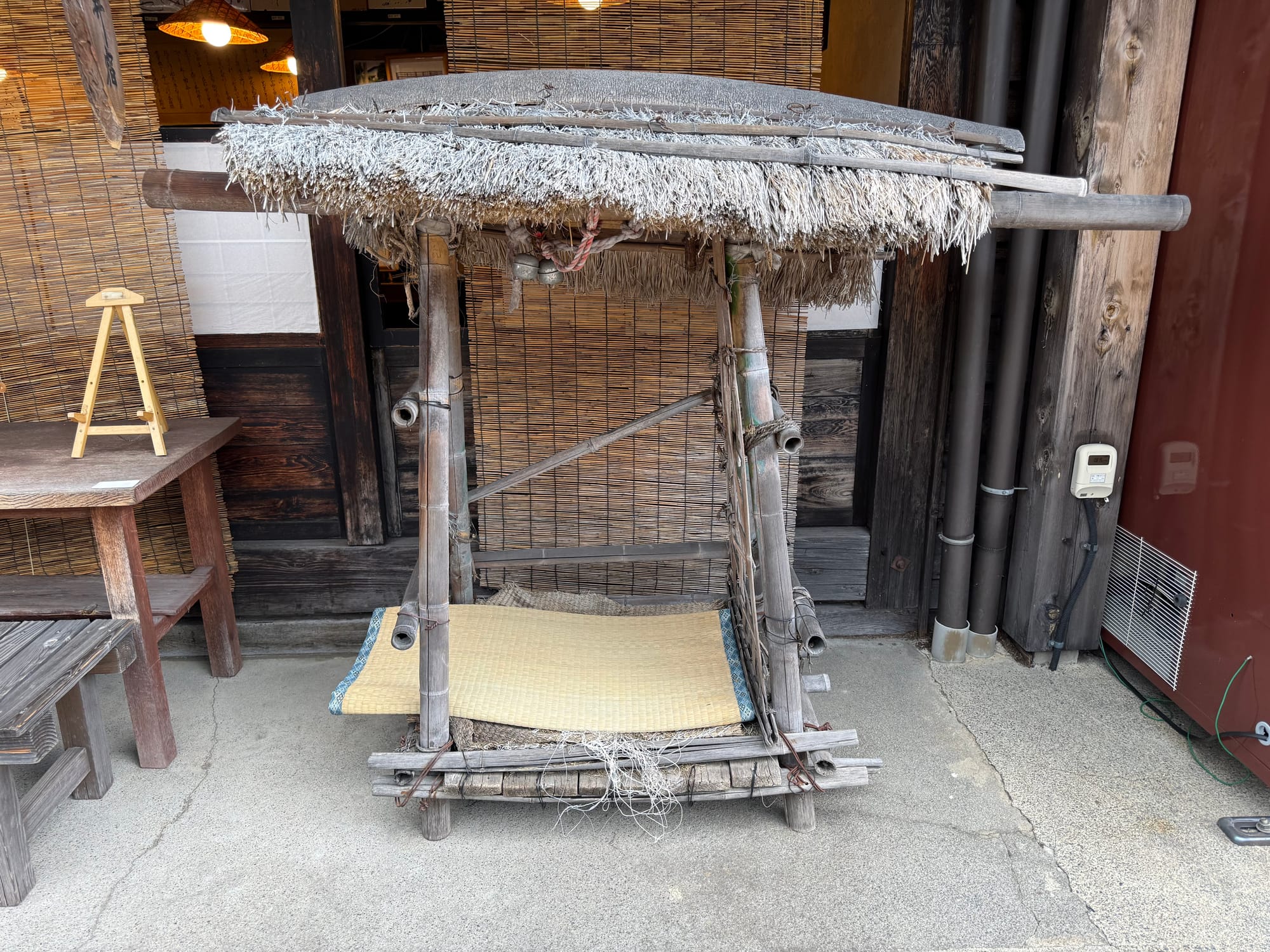 Traditional one-person palanquin displayed in Narai-juku, constructed from wood, bamboo and thatch, with carrying poles and a woven seat used for mountain travel.