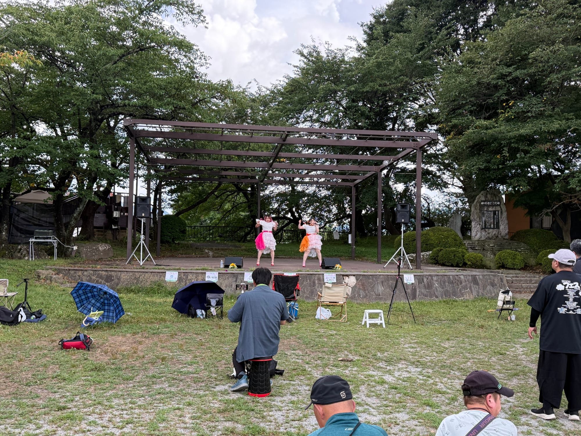 Idol performance at Takashima Castle Fes in Suwa, with two performers dancing on an outdoor stage while visitors watch from the lawn in front of the castle grounds.
