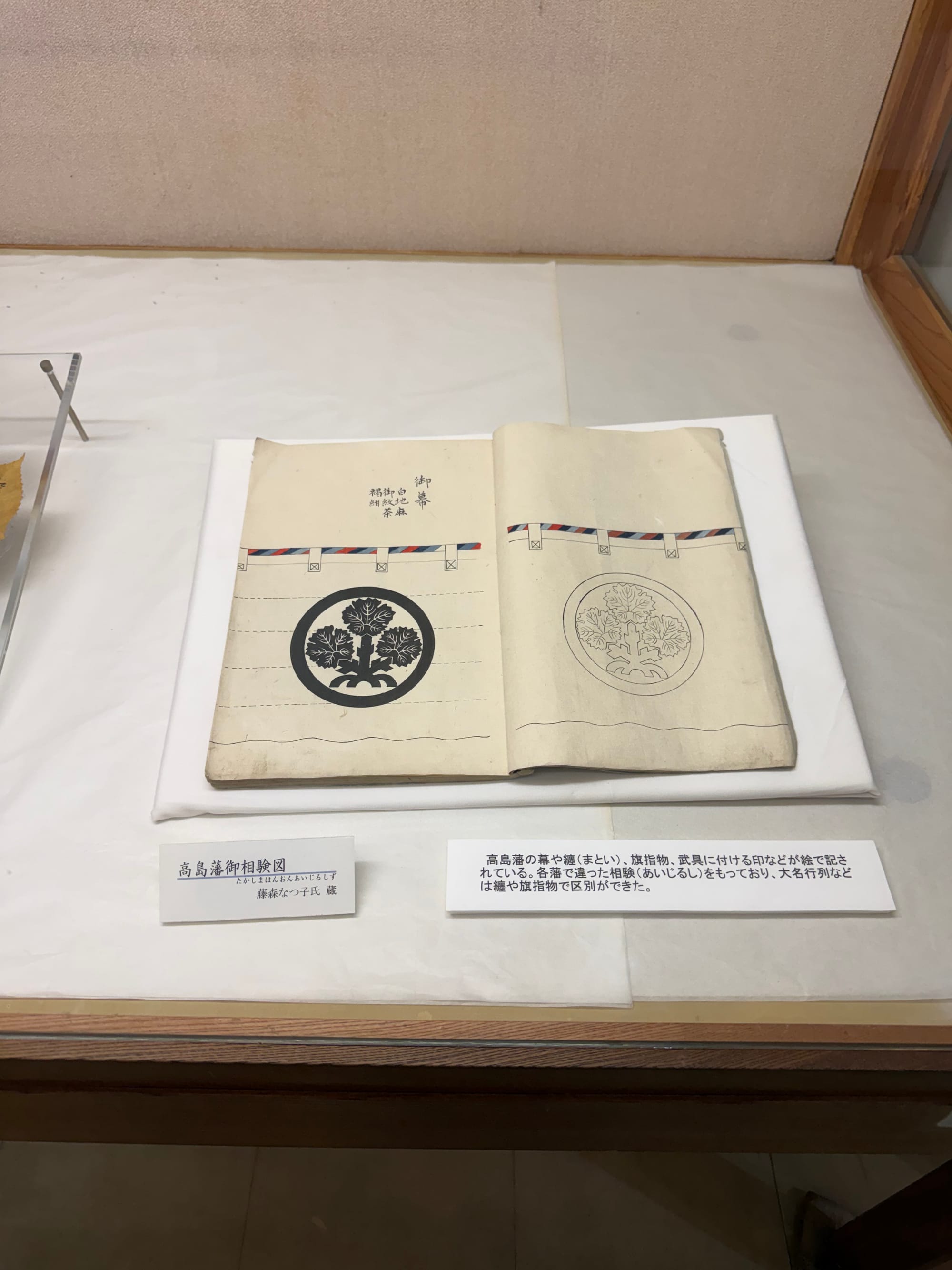 Historic document displayed at Takashima Castle, showing the crest of the Suwa clan and illustrations of heraldic emblems used on banners, armour and military equipment.