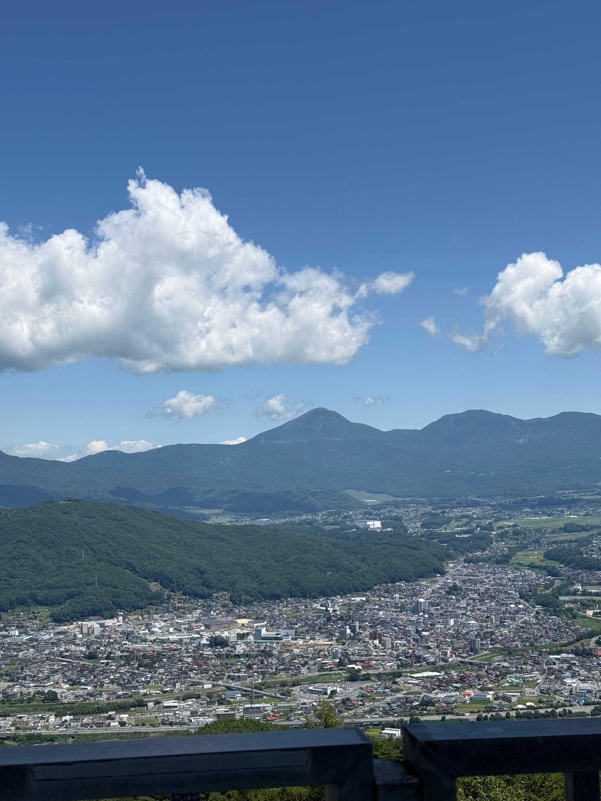 View from the Tsuetsukitoge Observation Deck overlooking the Suwa Basin, with Mt Tateshina rising in the distance above towns, forests and farmland beneath a clear blue sky.