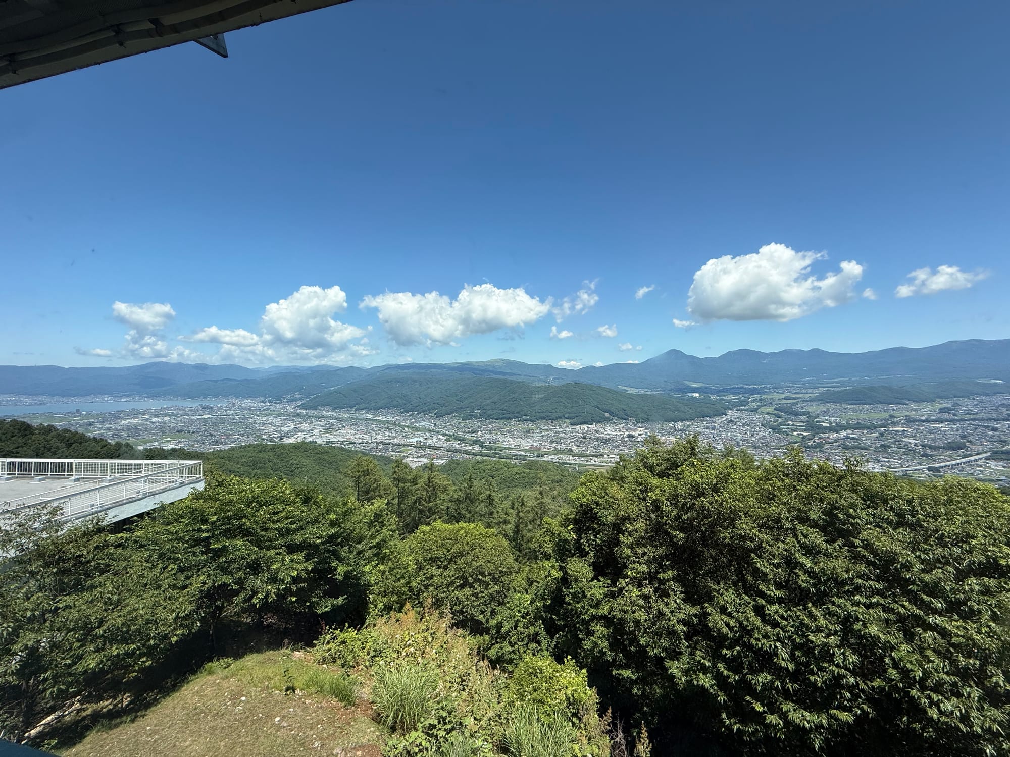 Panoramic view from the Tsuetsukitoge Observation Deck restaurant, overlooking the Suwa Basin, Lake Suwa, Mt Tateshina and surrounding mountains beneath a clear blue sky.