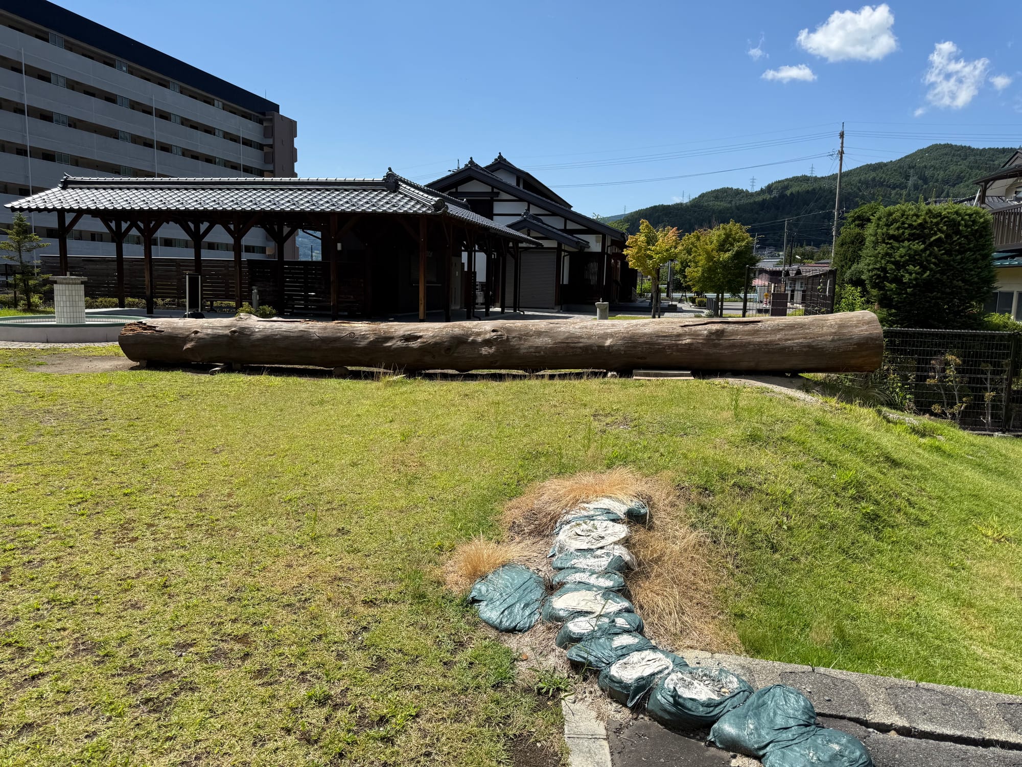 Copilot said:  Alt text (191 characters or under):  Large Onbashira log displayed outside Onbashira-kan Yoisa in Shimosuwa, showing one of the massive sacred pillars used in the Suwa Grand Shrine's Onbashira Festival.