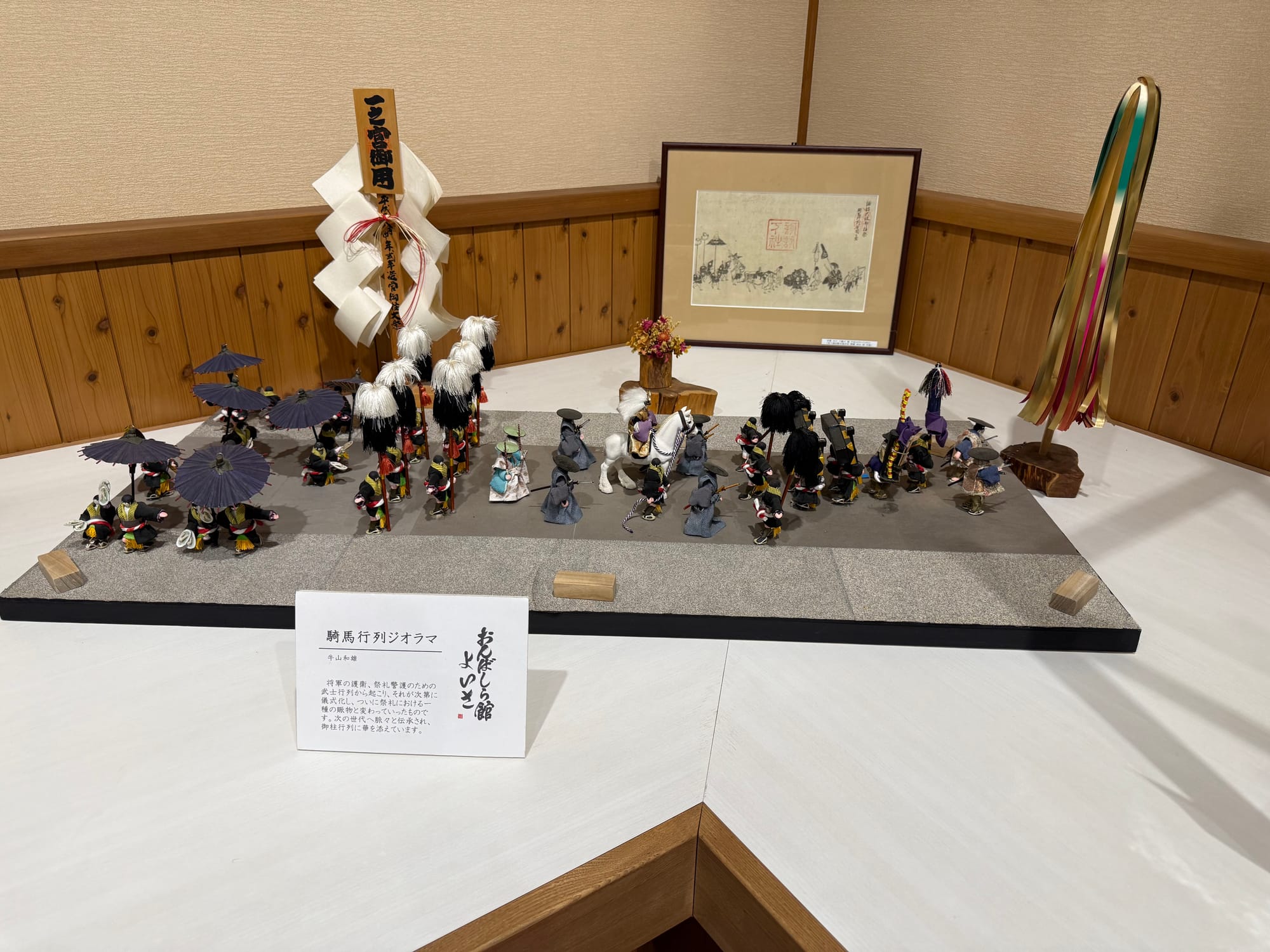 Diorama at Onbashira-kan Yoisa depicting a traditional Suwa festival procession, with miniature figures, ceremonial banners, umbrellas, musicians and a mounted participant.