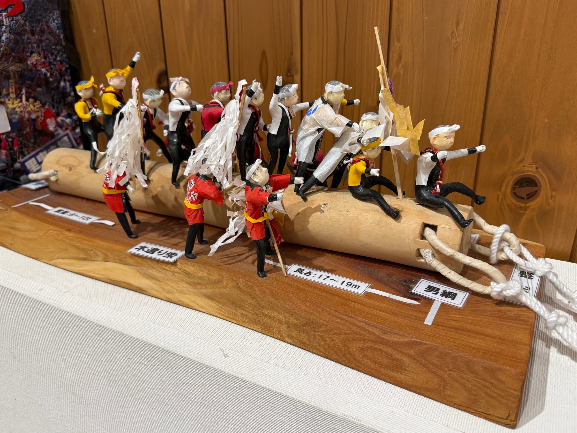 Scale model at Onbashira-kan Yoisa showing participants riding and guiding an Onbashira log during the festival, with ropes, ceremonial figures and traditional dress.