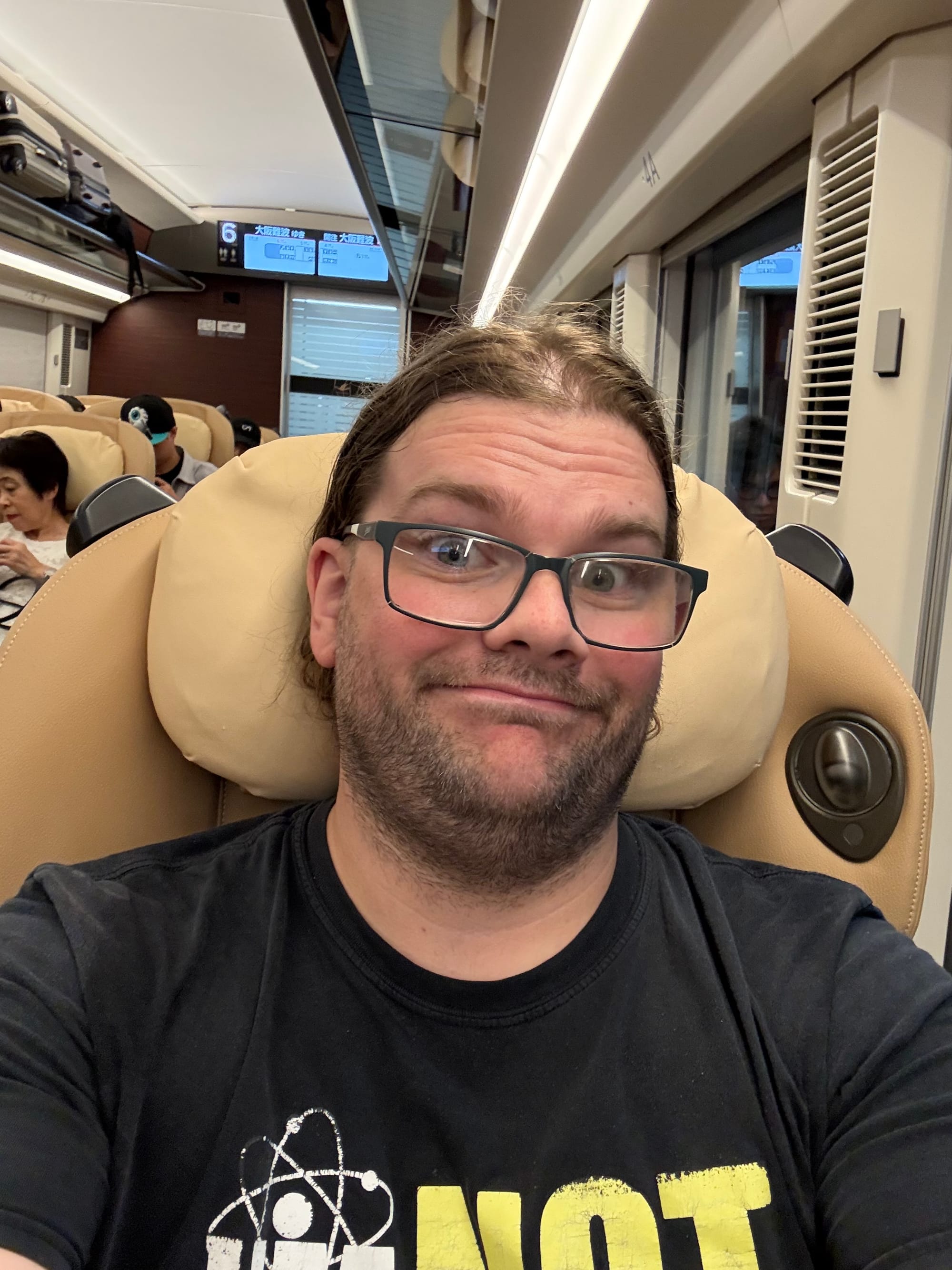 Passenger seated in a premium seat aboard a Kintetsu Hinotori limited express train, with the spacious carriage interior, reclining seats and onboard displays visible.