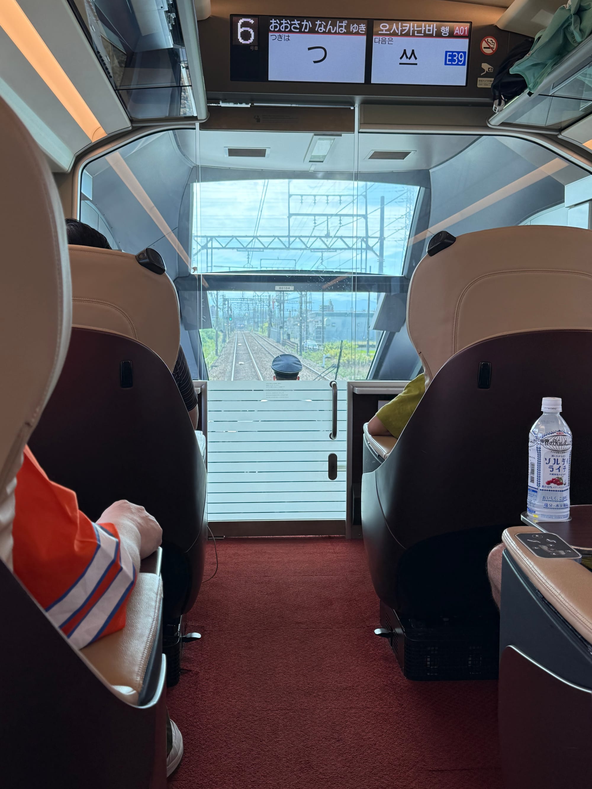 View from the front observation seats of a Kintetsu Hinotori limited express train, showing the driver's cab window, railway tracks ahead and the train's spacious premium interior.