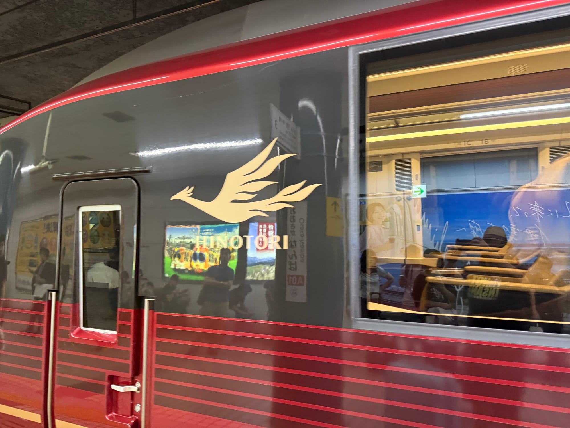 Kintetsu 80000 series Hinotori limited express train at a station platform, showing its distinctive metallic red bodywork and gold phoenix emblem on the side of the carriage.