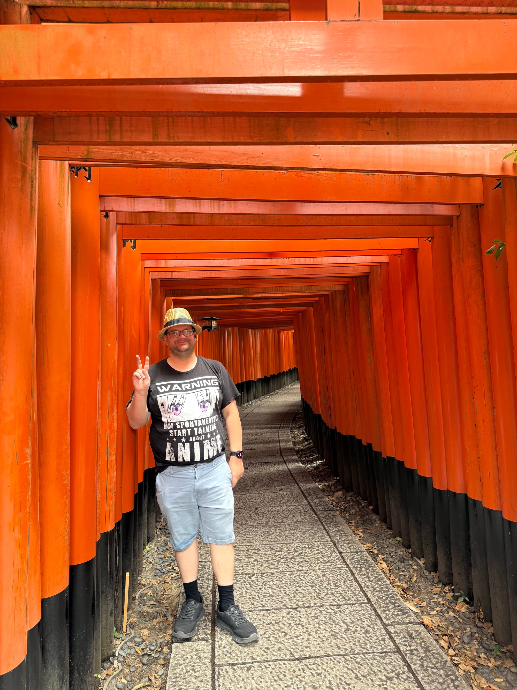 Visitor standing within the vermilion torii gate tunnels of Fushimi Inari Taisha, posing on the stone pathway as rows of closely spaced gates curve into the distance.
