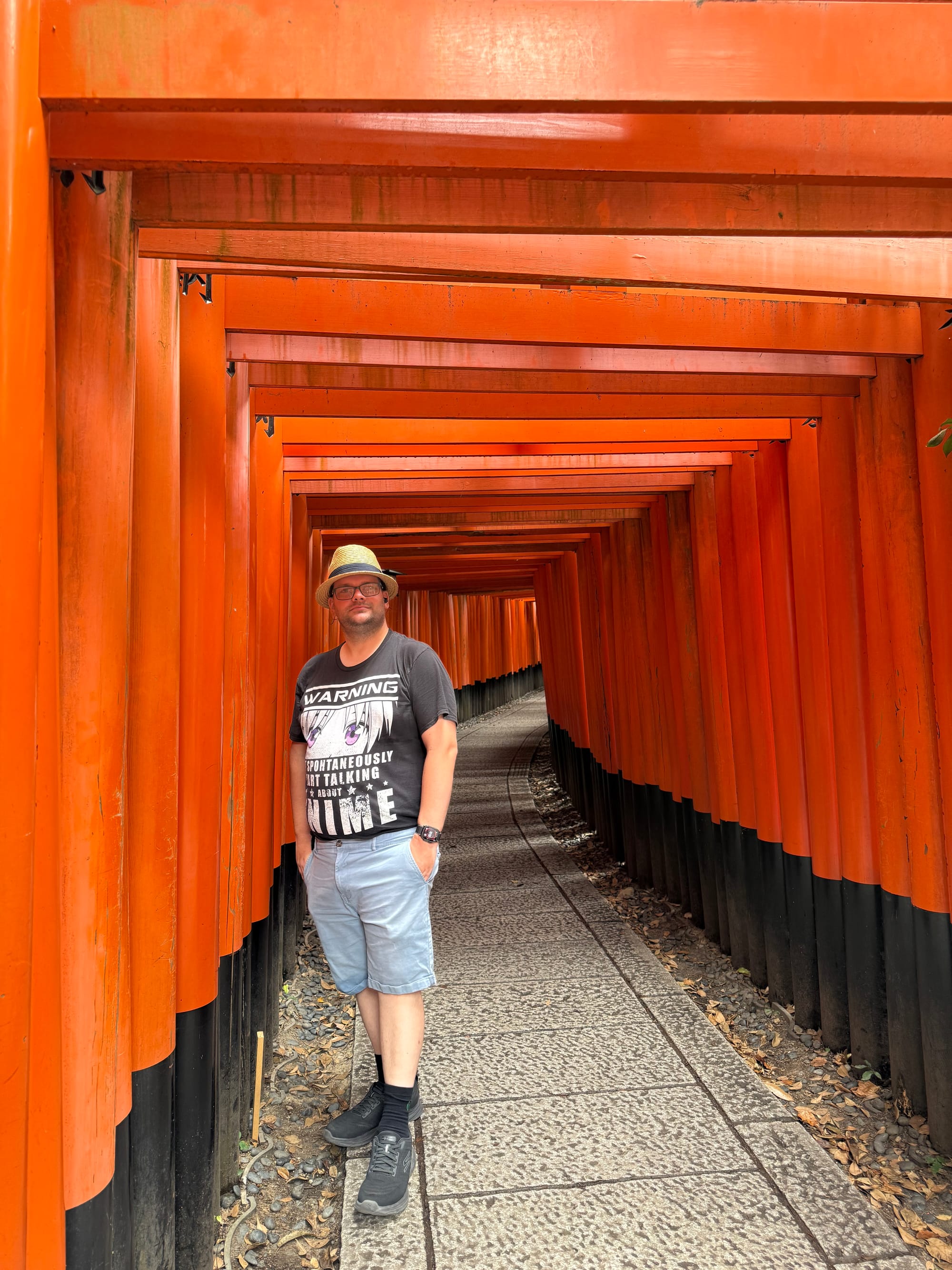 Visitor standing within the vermilion torii tunnels of Fushimi Inari Taisha, beside the narrow stone pathway as rows of closely spaced gates curve through the shrine grounds.
