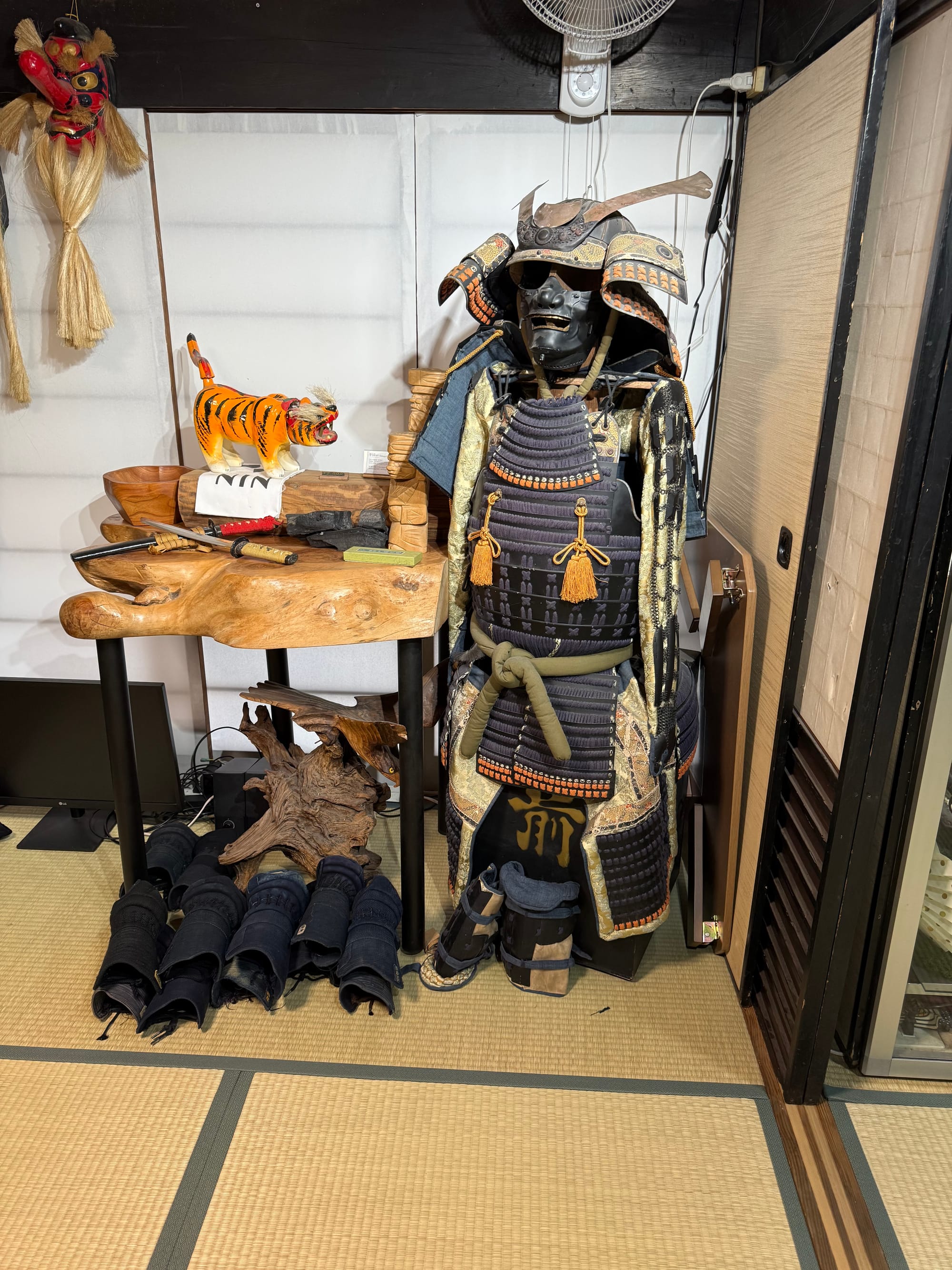 Traditional Japanese samurai armour displayed in a tatami room in Kyoto, alongside kendo equipment, wooden weapons, decorative masks and martial arts training gear.