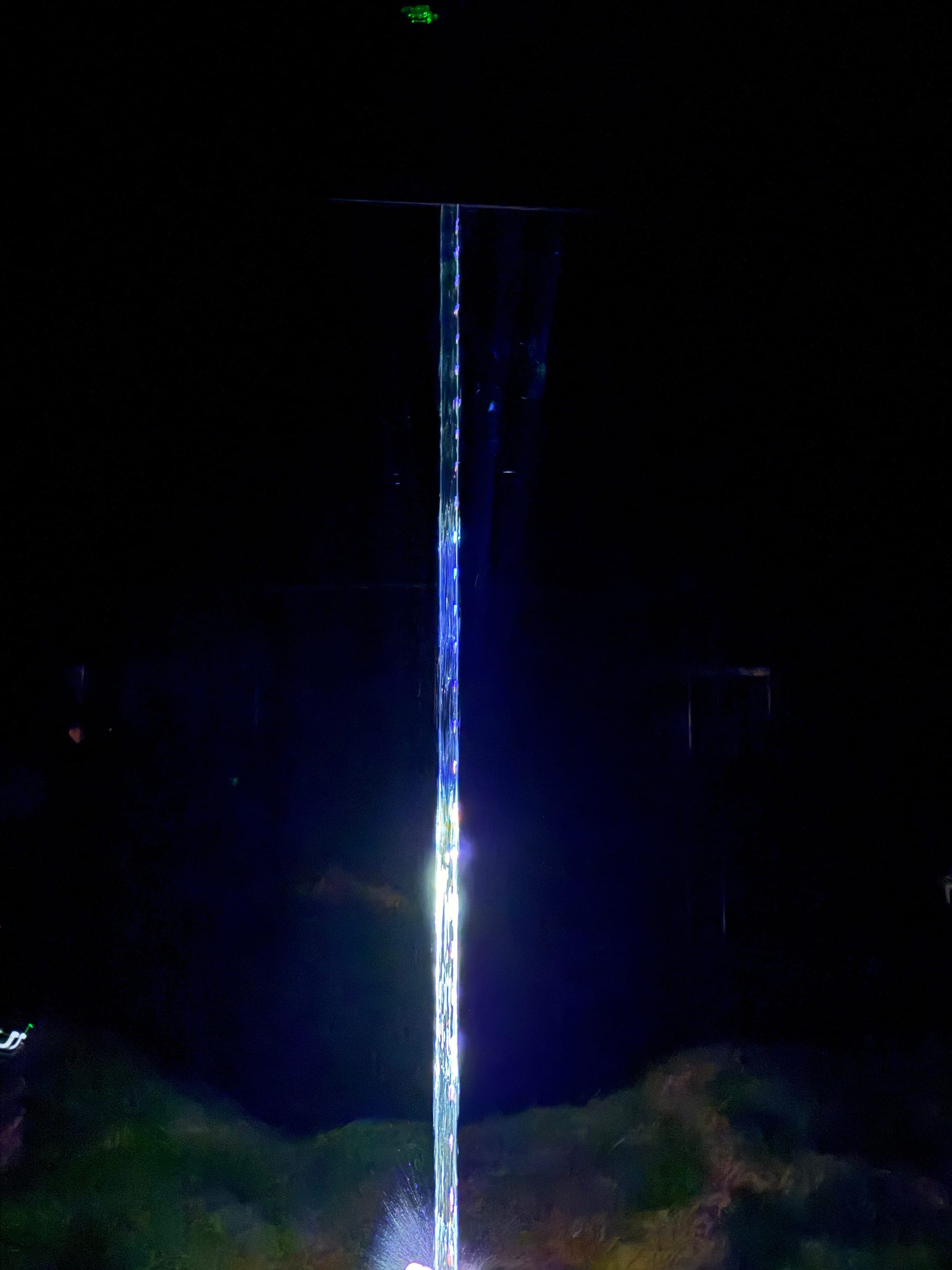 Ephemeral Crystallized Drop at teamLab Biovortex Kyoto, featuring a towering column of shimmering light rising from a glowing base within a dark immersive gallery space.