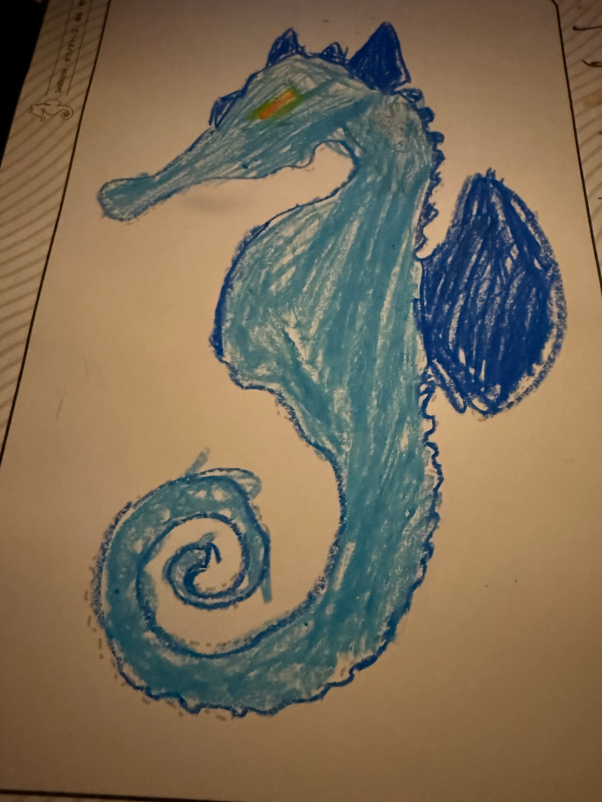 Hand-drawn blue seahorse-like dragon created by a visitor at teamLab Future Park, featuring a curled tail, dark blue fins and a brightly coloured eye on a white page.