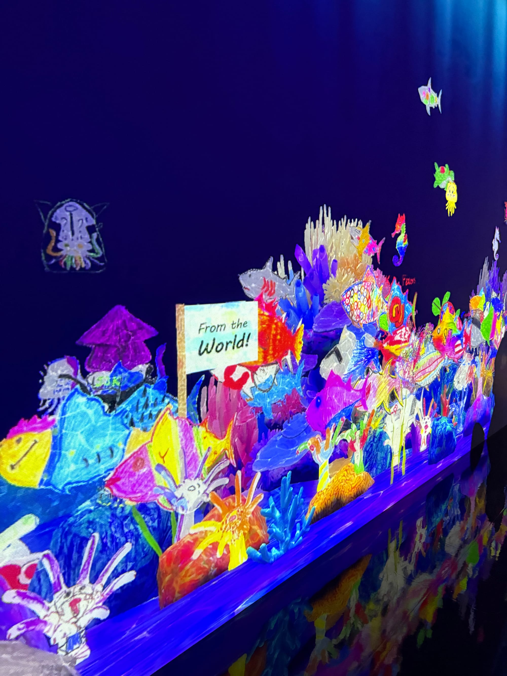 Interactive digital ocean at teamLab Future Park, filled with colourful sea creatures created from visitors' drawings, including fish, squid and coral-inspired designs.