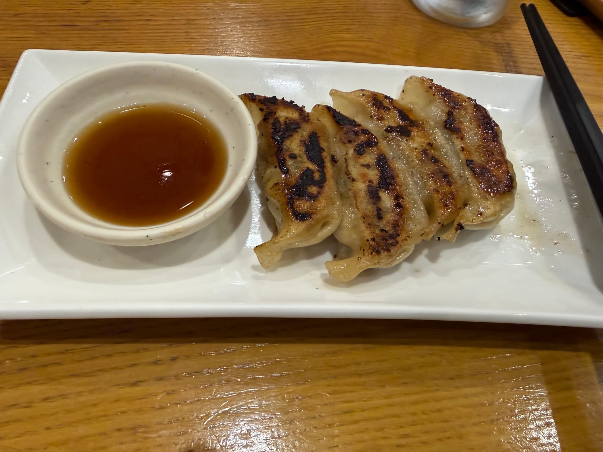 Pan-fried gyoza dumplings served on a rectangular plate with a dipping sauce, showing crisp golden-brown skins and charred grill marks at a restaurant in Japan.