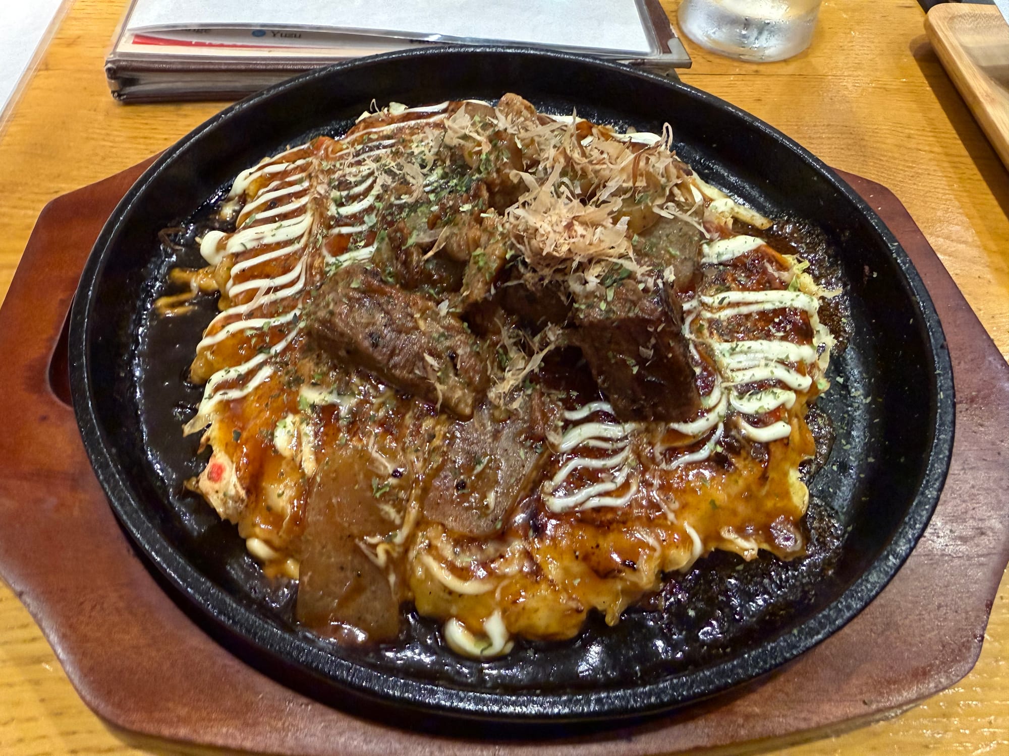 Beef tenderloin okonomiyaki served on a hot iron plate, topped with grilled beef, okonomiyaki sauce, mayonnaise, bonito flakes and dried seaweed at a restaurant in Japan.