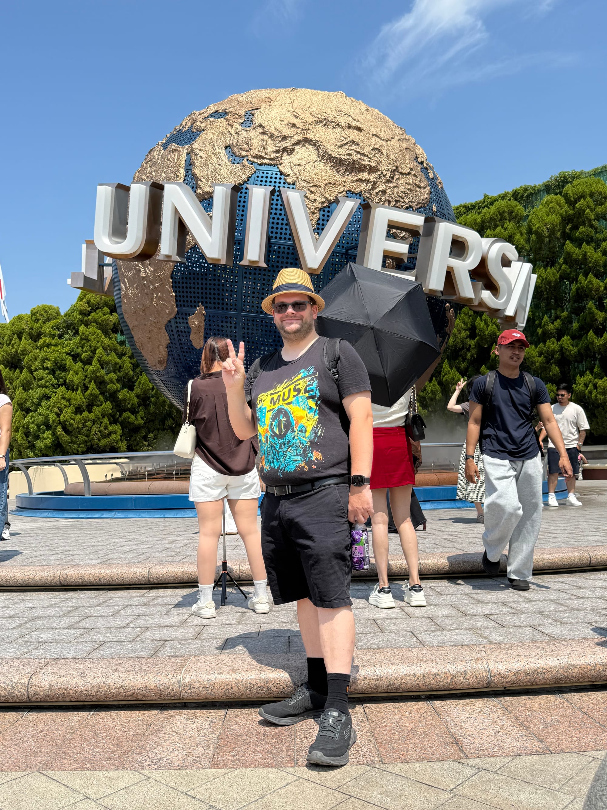 Visitor posing in front of the Universal Studios globe at Universal Studios Japan in Osaka, with the iconic rotating landmark, fountains and park entrance plaza behind.