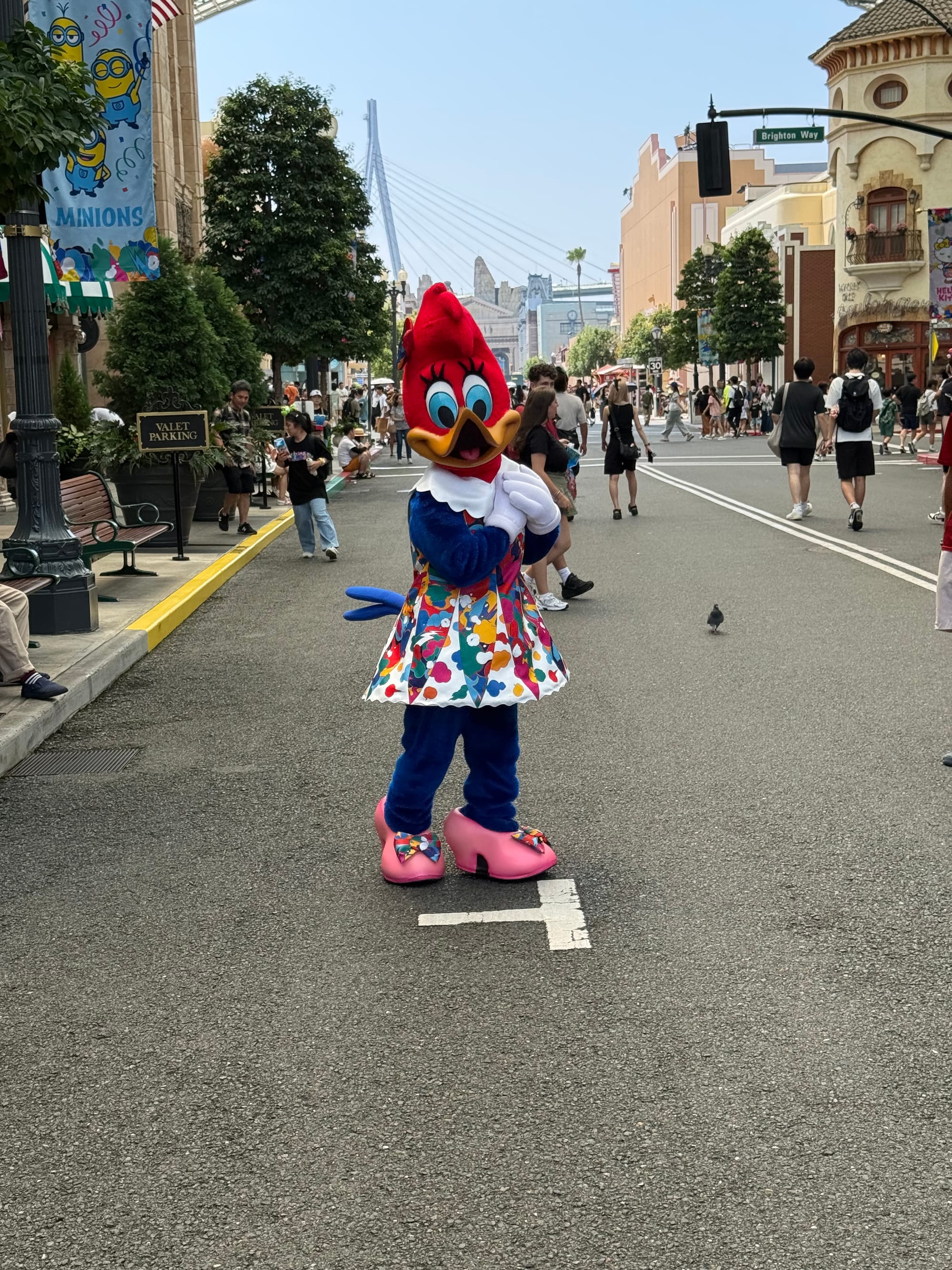 Woody Woodpecker character performer at Universal Studios Japan, standing on a themed Hollywood street in a colourful anniversary outfit with visitors and park buildings in the background.