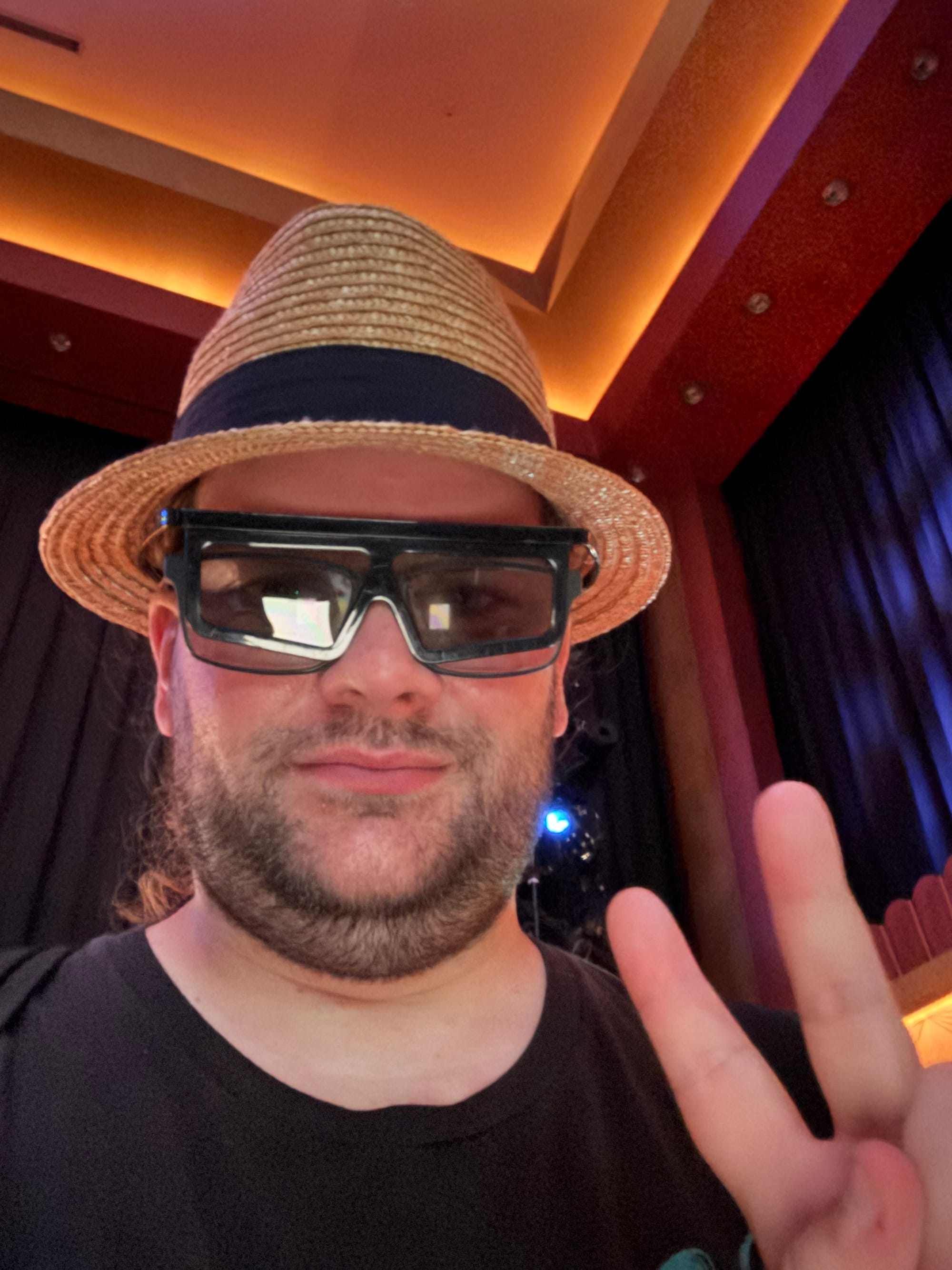 Visitor wearing 3D glasses and a straw hat inside a Universal Studios Japan attraction, posing with a peace sign in a dimly lit theatre featuring warm orange lighting.