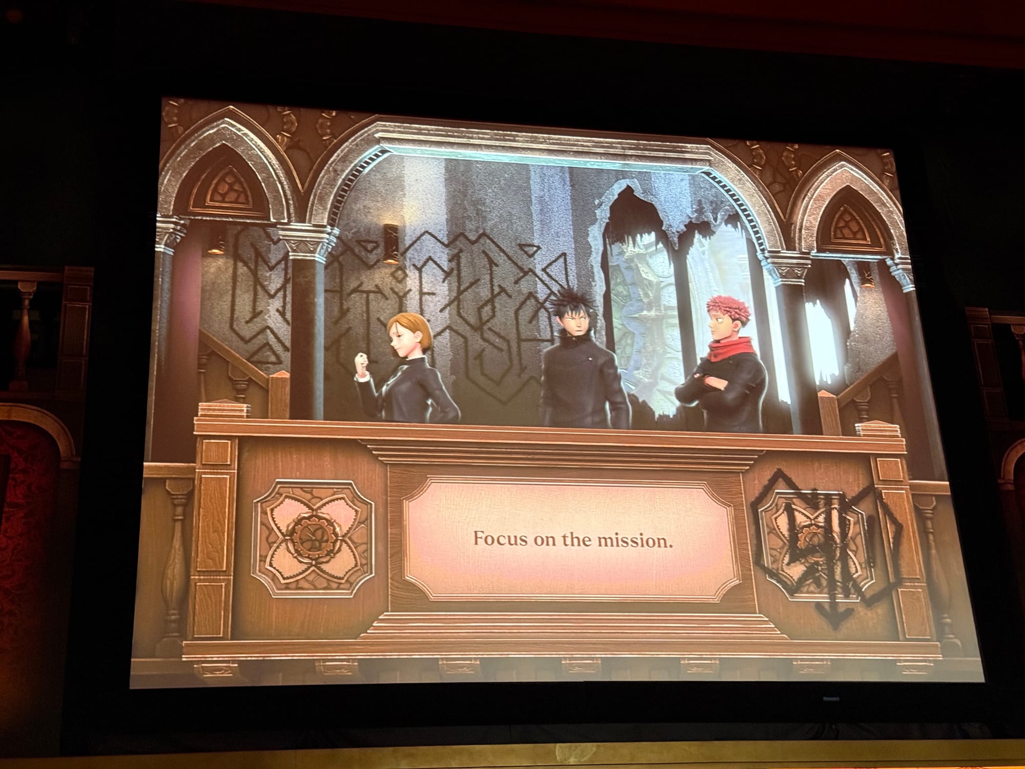 Screen inside Jujutsu Kaisen: The Real 4-D at Universal Studios Japan, showing Yuji Itadori, Megumi Fushiguro and Nobara Kugisaki delivering a mission briefing.