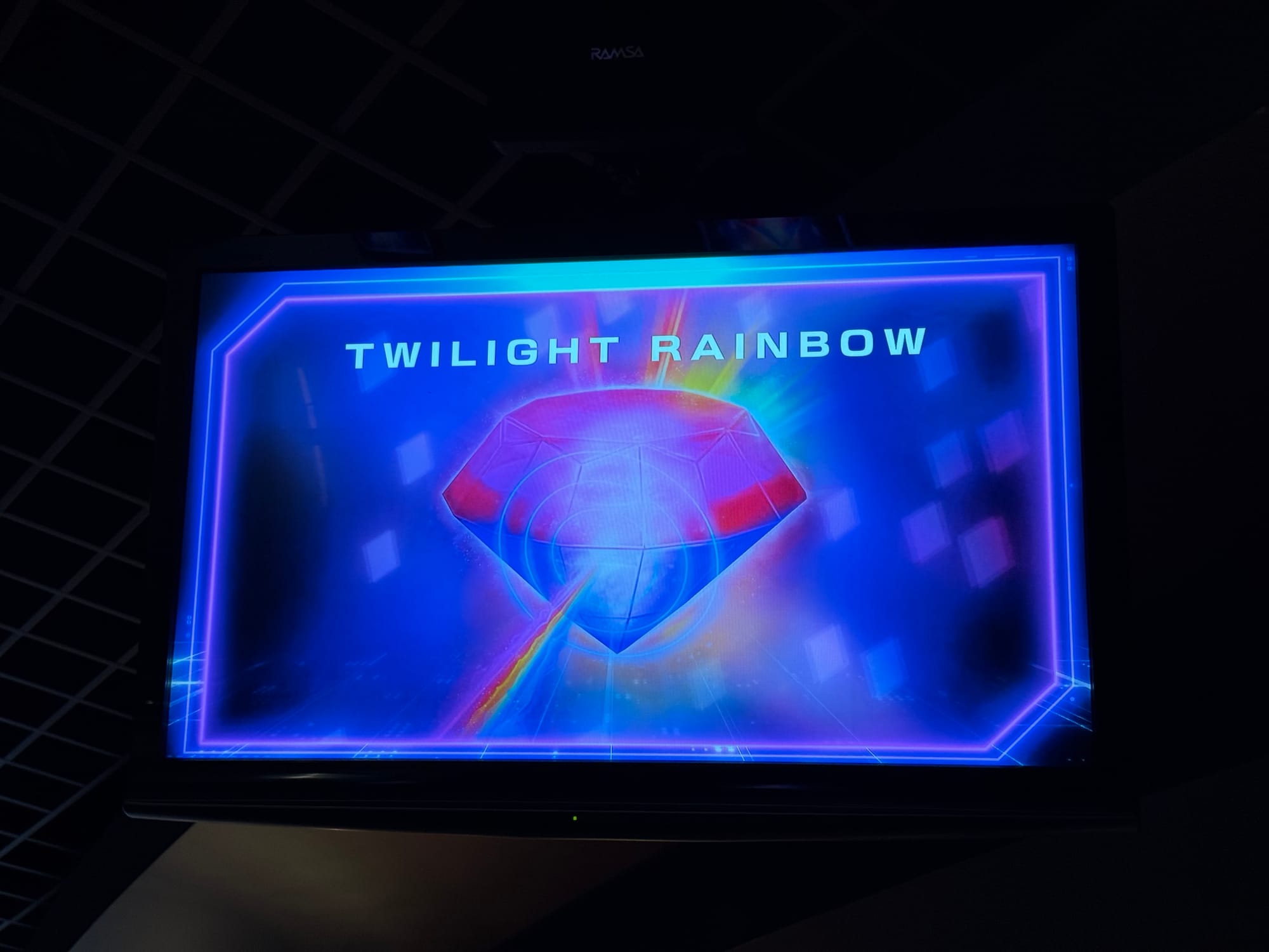 Monitor inside Mario Kart: Koopa's Challenge displaying the Rainbow Road trophy, labelled "Twilight Rainbow", with colourful light effects and futuristic racing graphics.