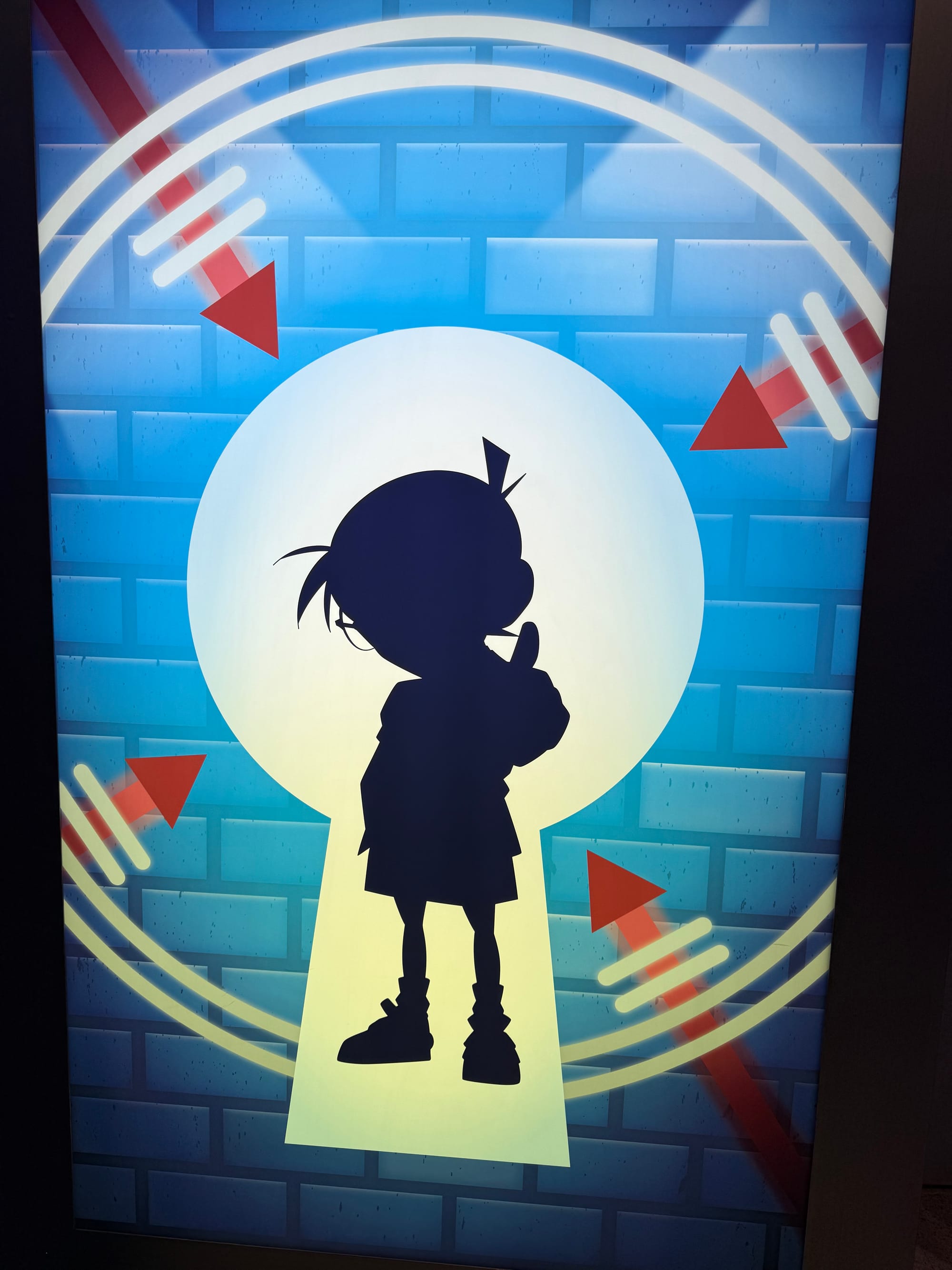 Silhouette of Detective Conan displayed within a glowing keyhole design at Universal Studios Japan, featuring the famous anime detective against a blue illuminated background.
