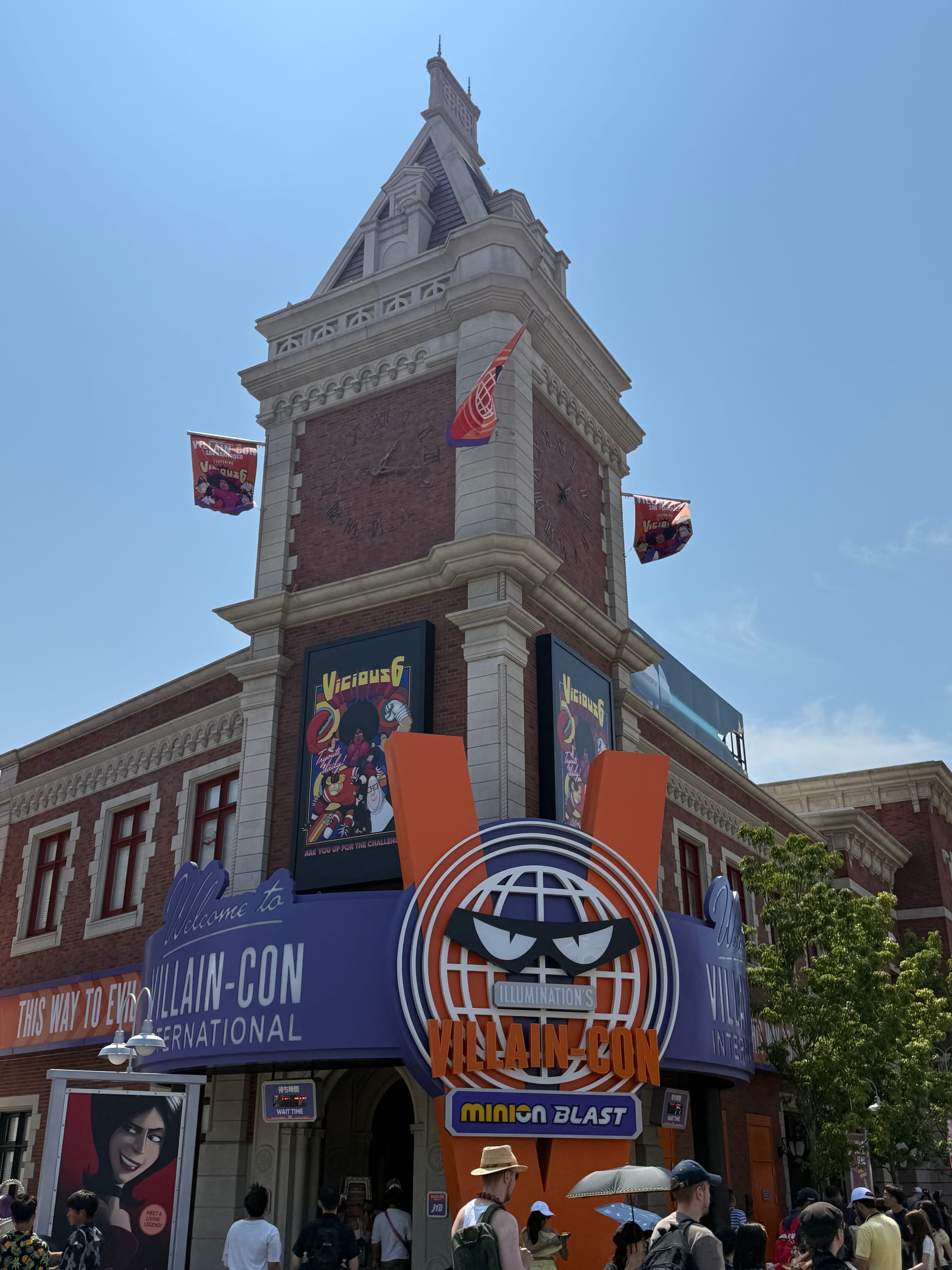 Entrance to Illumination's Villain-Con Minion Blast at Universal Studios Japan, featuring the Villain-Con façade, themed signage, banners and a clock tower above the attraction entrance.