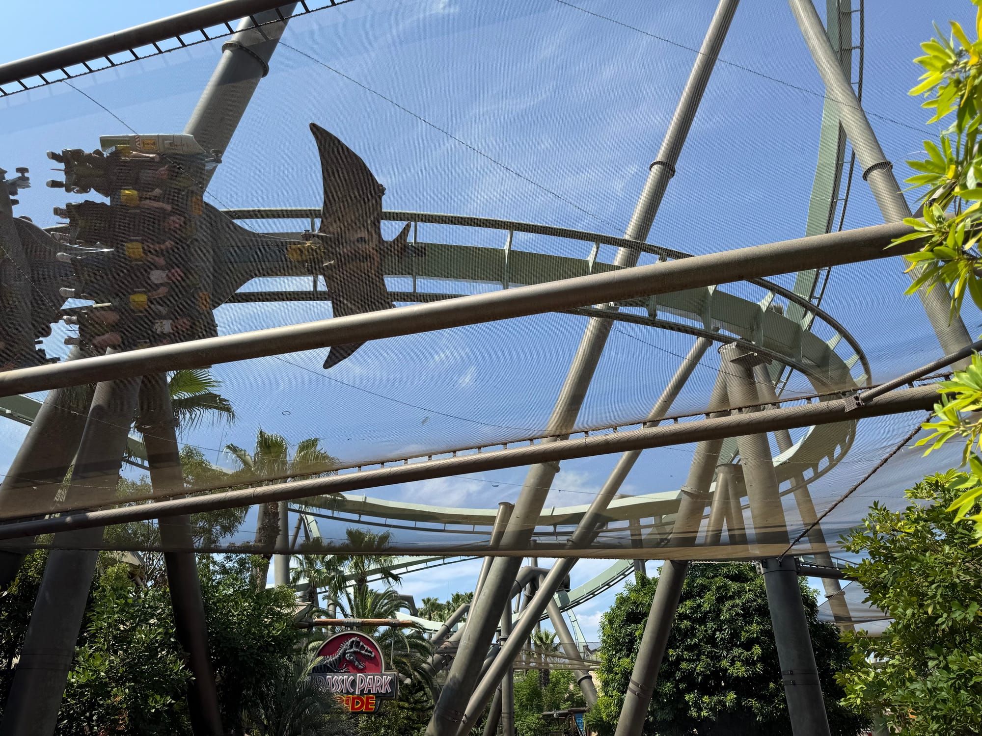 The Flying Dinosaur coaster train racing through a twisting section of track at Universal Studios Japan, with riders suspended face-down beneath the track in Jurassic Park.
