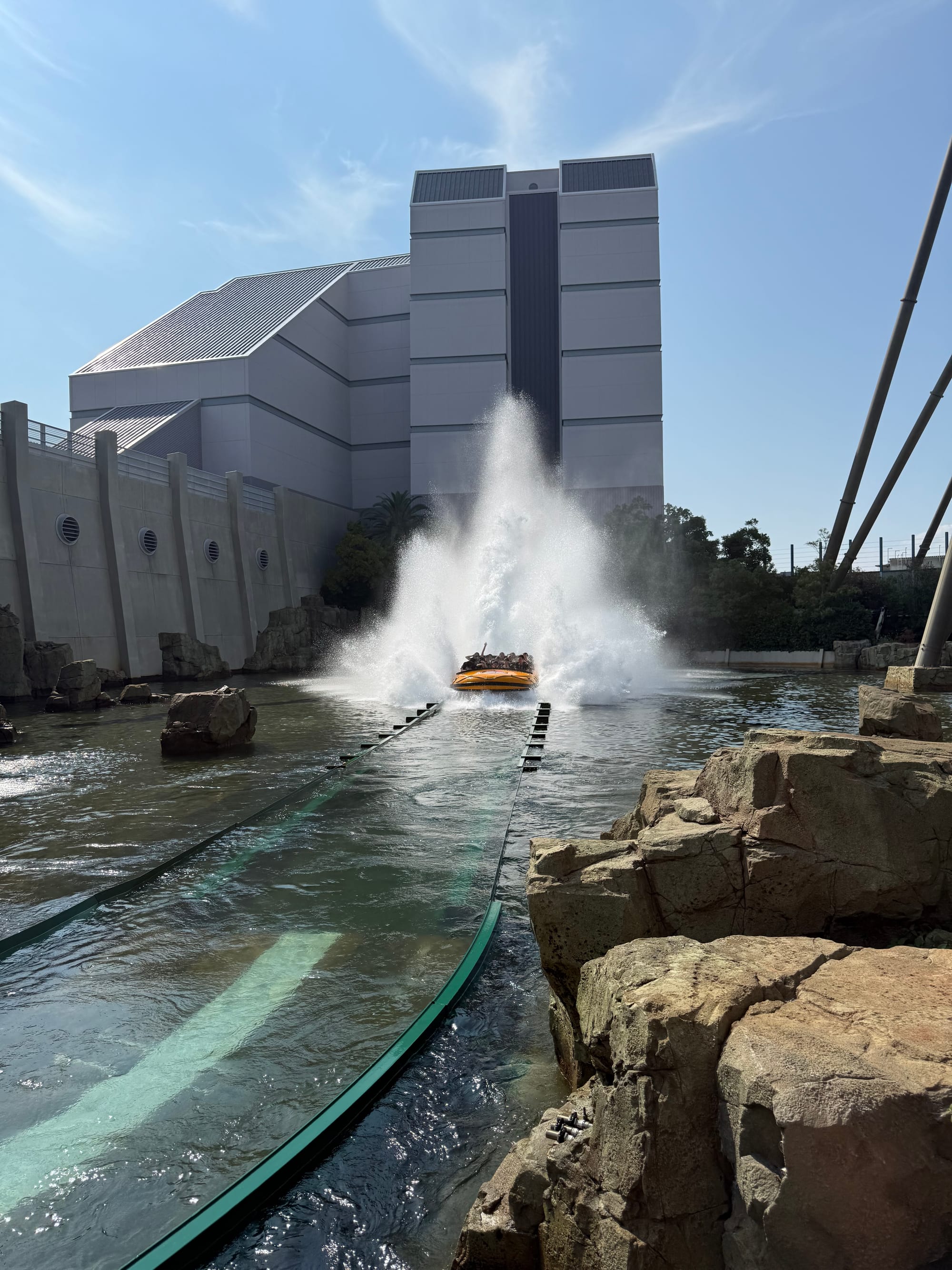 Boat plunging into the splashdown at Jurassic Park: The Ride at Universal Studios Japan, sending a huge wall of water into the air beside rocky landscaping and the attraction building.