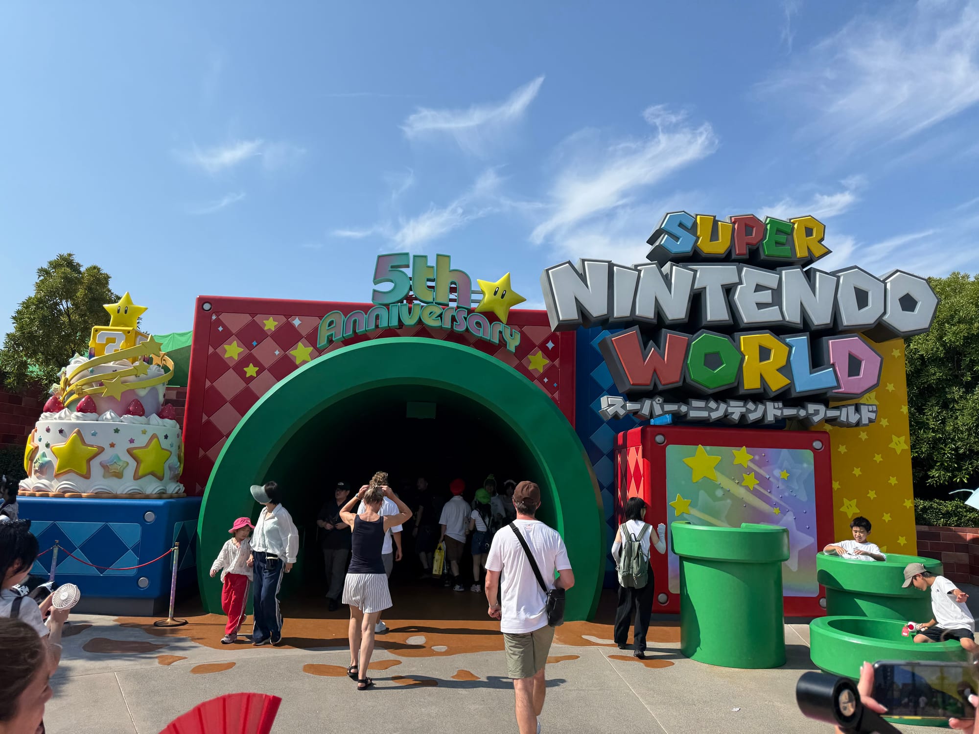 Entrance to Super Nintendo World at Universal Studios Japan, featuring a giant green warp pipe, colourful Mario-themed decorations and 5th anniversary signage.