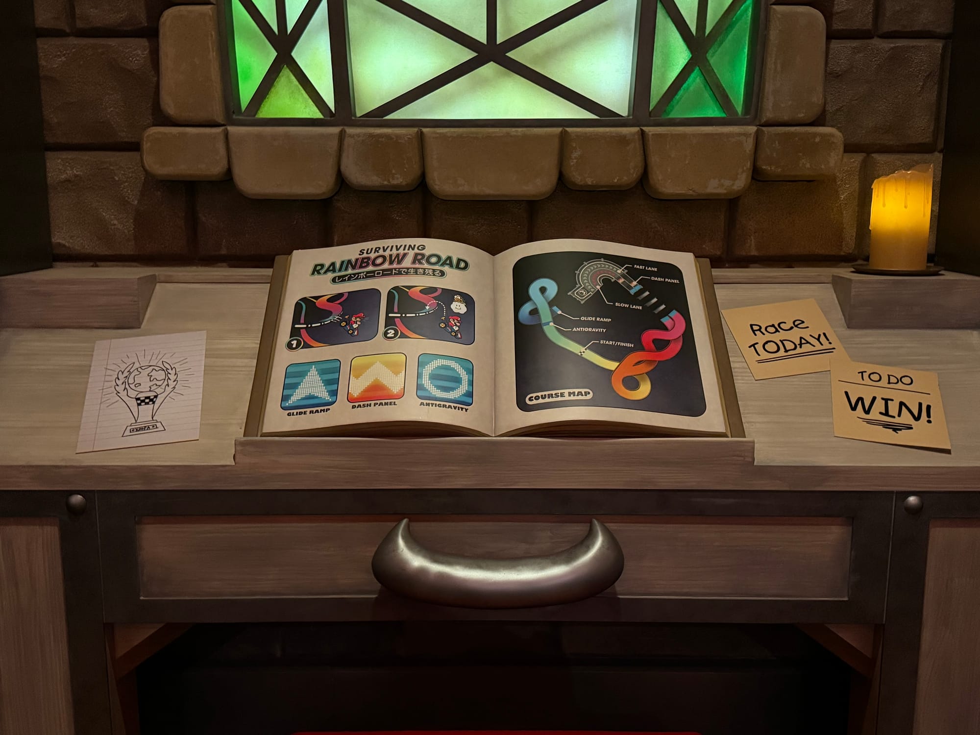 Open book display in Bowser's Castle at Mario Kart: Koopa's Challenge, showing a Rainbow Road course map, racing tips and themed notes within the attraction queue.