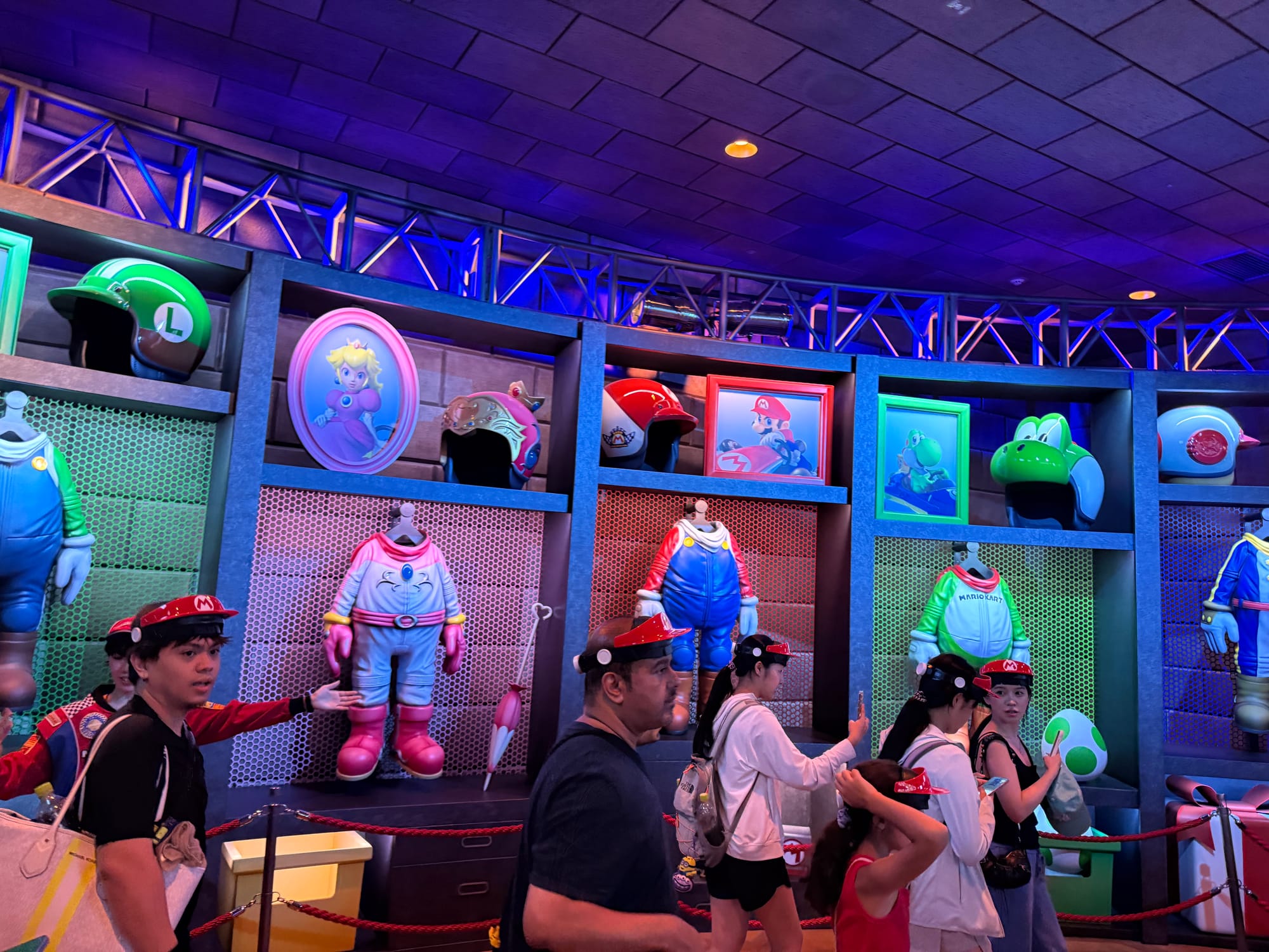Display of Mario Kart racing suits, helmets and character equipment inside Mario Kart: Koopa's Challenge at Super Nintendo World, with guests walking through the themed queue.