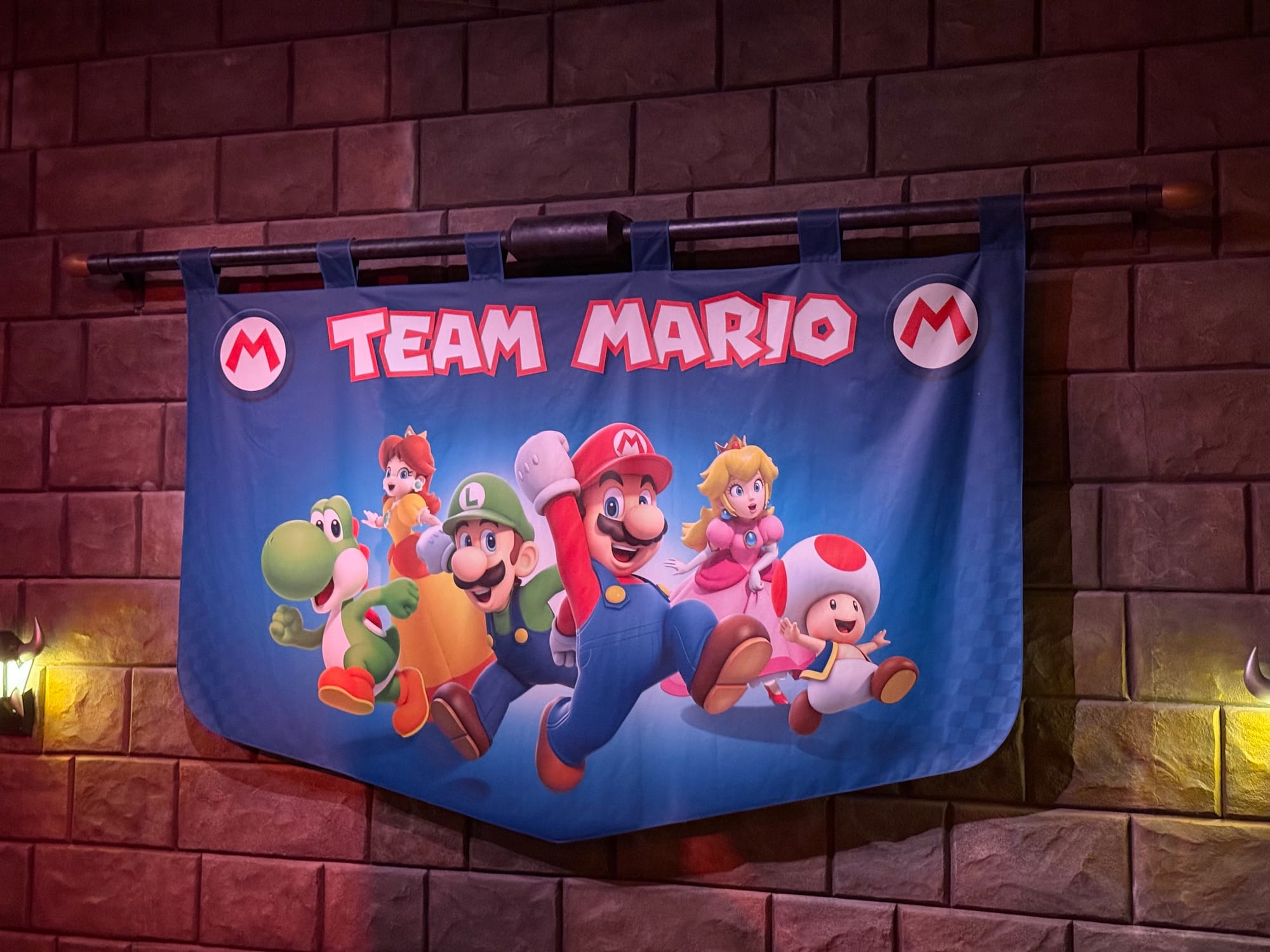 Team Mario banner inside Mario Kart: Koopa's Challenge at Super Nintendo World, featuring Mario, Luigi, Peach, Daisy, Yoshi and Toad displayed on a castle wall.