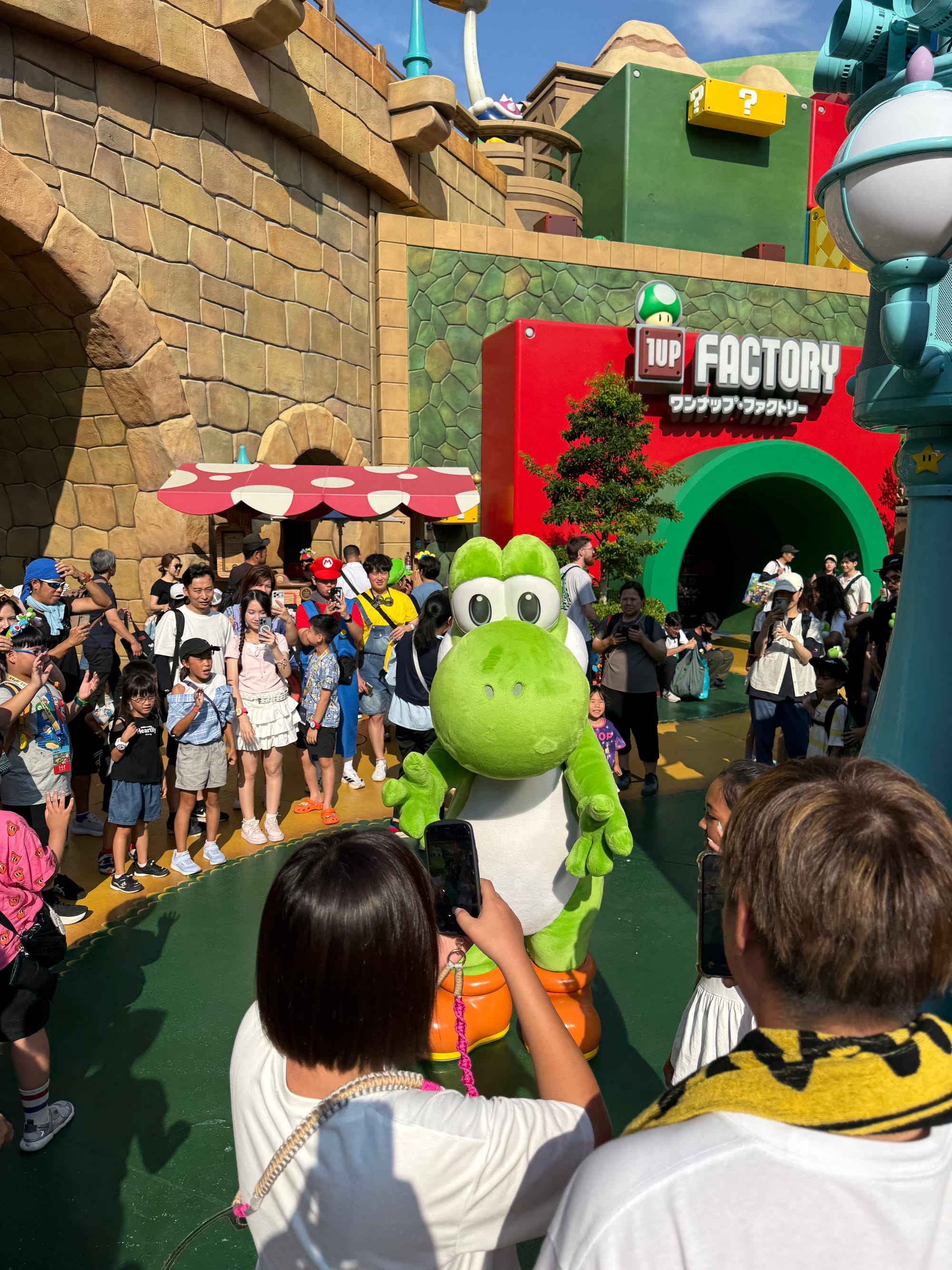 Mario and Luigi character performers greet visitors in Super Nintendo World at Universal Studios Japan, surrounded by themed scenery inspired by the Mushroom Kingdom.