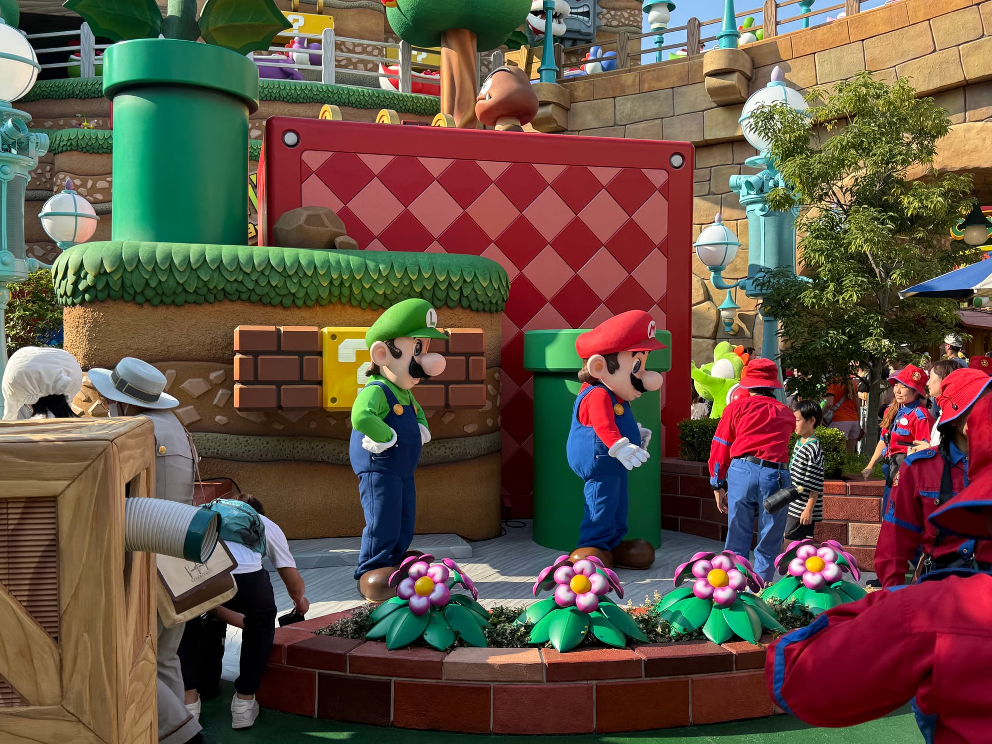 Mario and Luigi character performers greet visitors in Super Nintendo World at Universal Studios Japan, surrounded by themed scenery inspired by the Mushroom Kingdom.