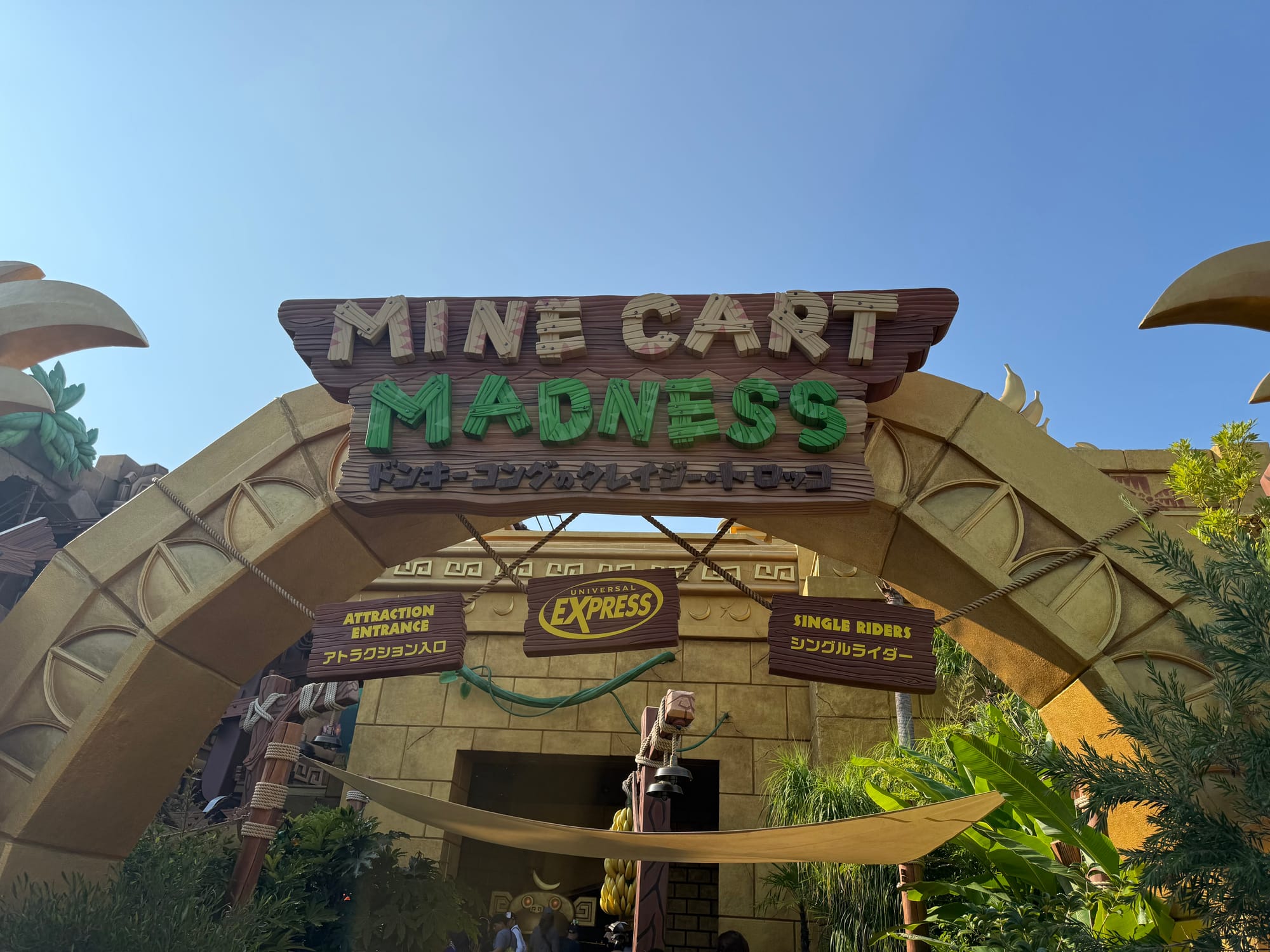 Entrance arch for Mine Cart Madness in Donkey Kong Country at Universal Studios Japan, featuring themed stonework, jungle foliage and attraction entrance signs beneath a clear blue sky.