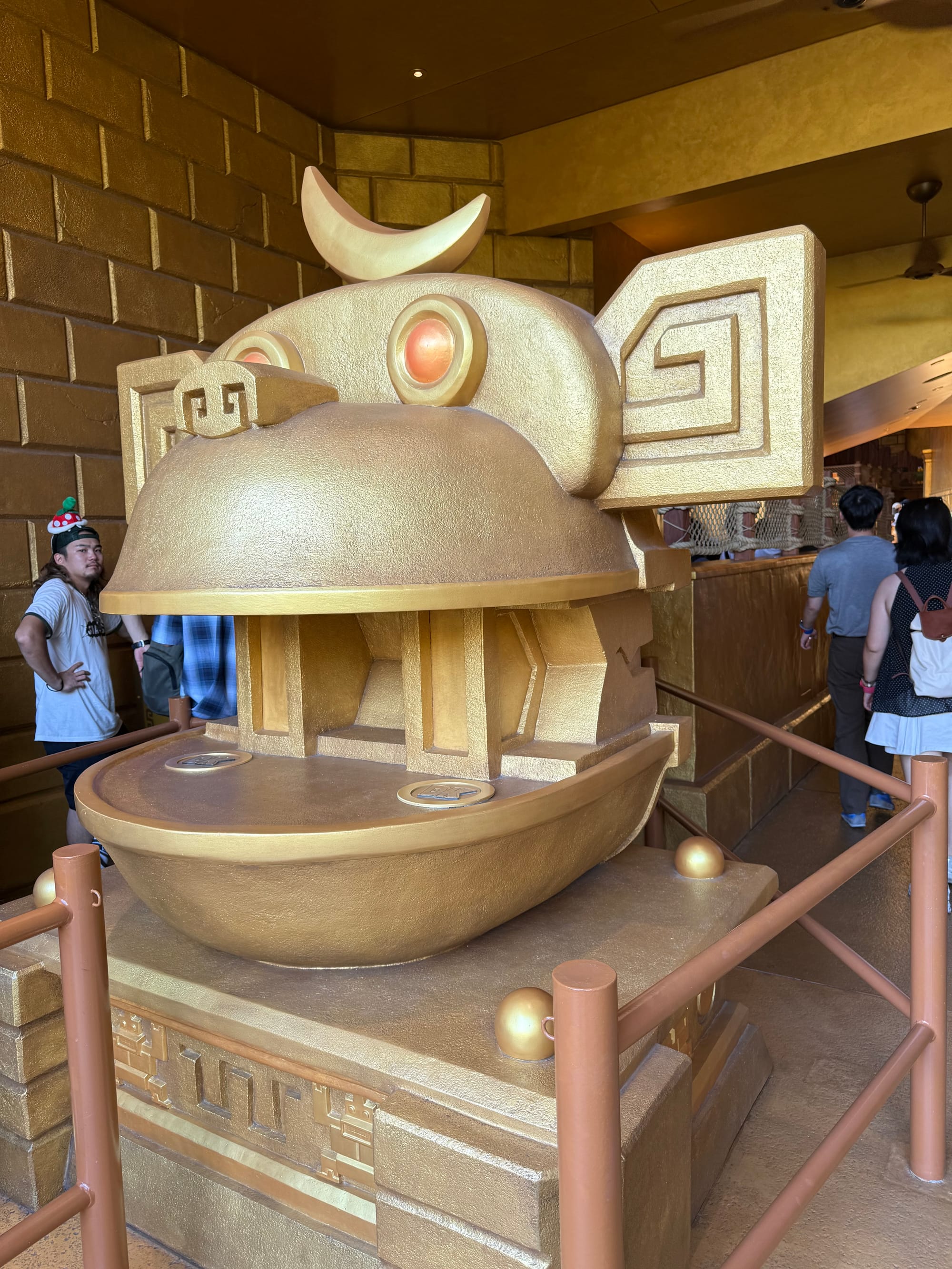 Golden temple statue in the queue for Mine Cart Madness at Donkey Kong Country, featuring a stylised ape face with glowing eyes, geometric carvings and themed jungle architecture.
