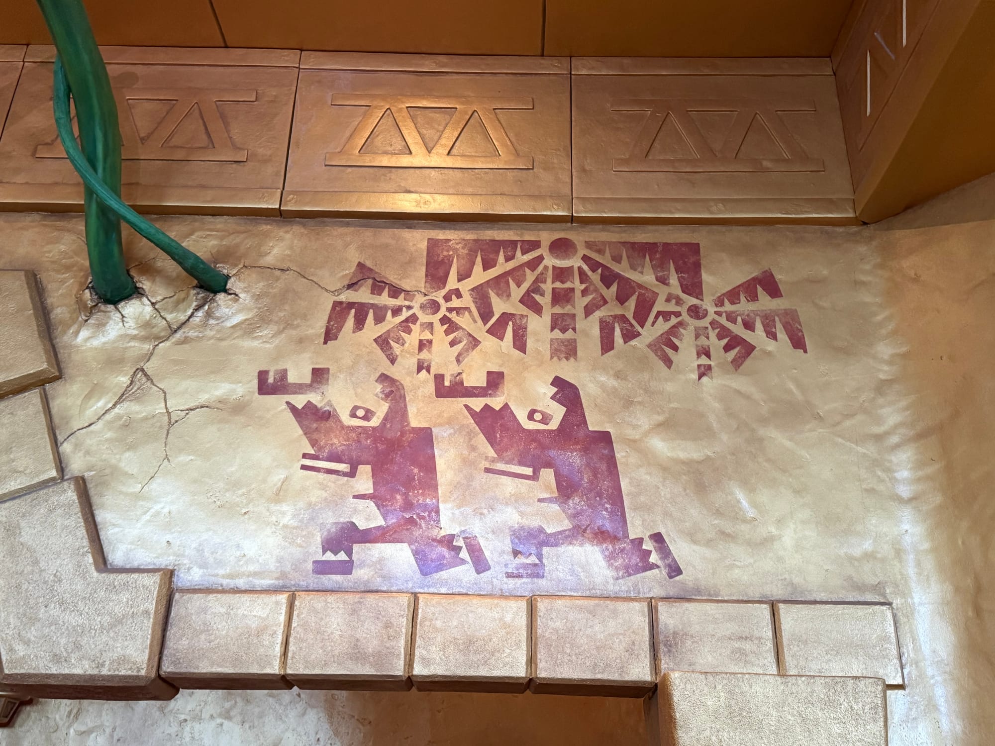 Temple-style mural in the queue for Mine Cart Madness at Donkey Kong Country, featuring stylised ape figures, geometric patterns and ancient jungle artwork on a stone wall.