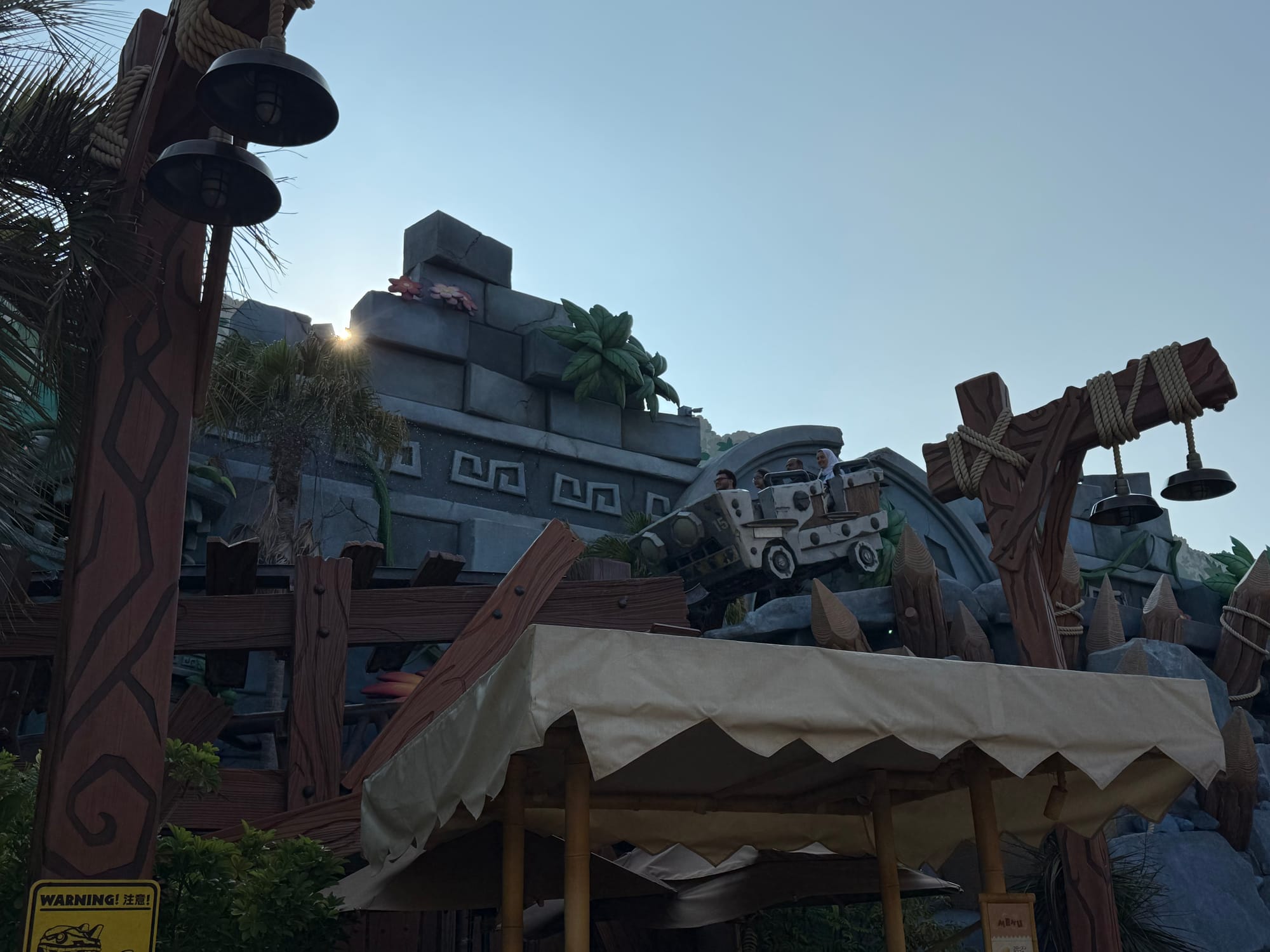 Mine cart train racing through Donkey Kong Country at Universal Studios Japan, appearing to leap a broken section of track beside jungle ruins, themed structures and rockwork.