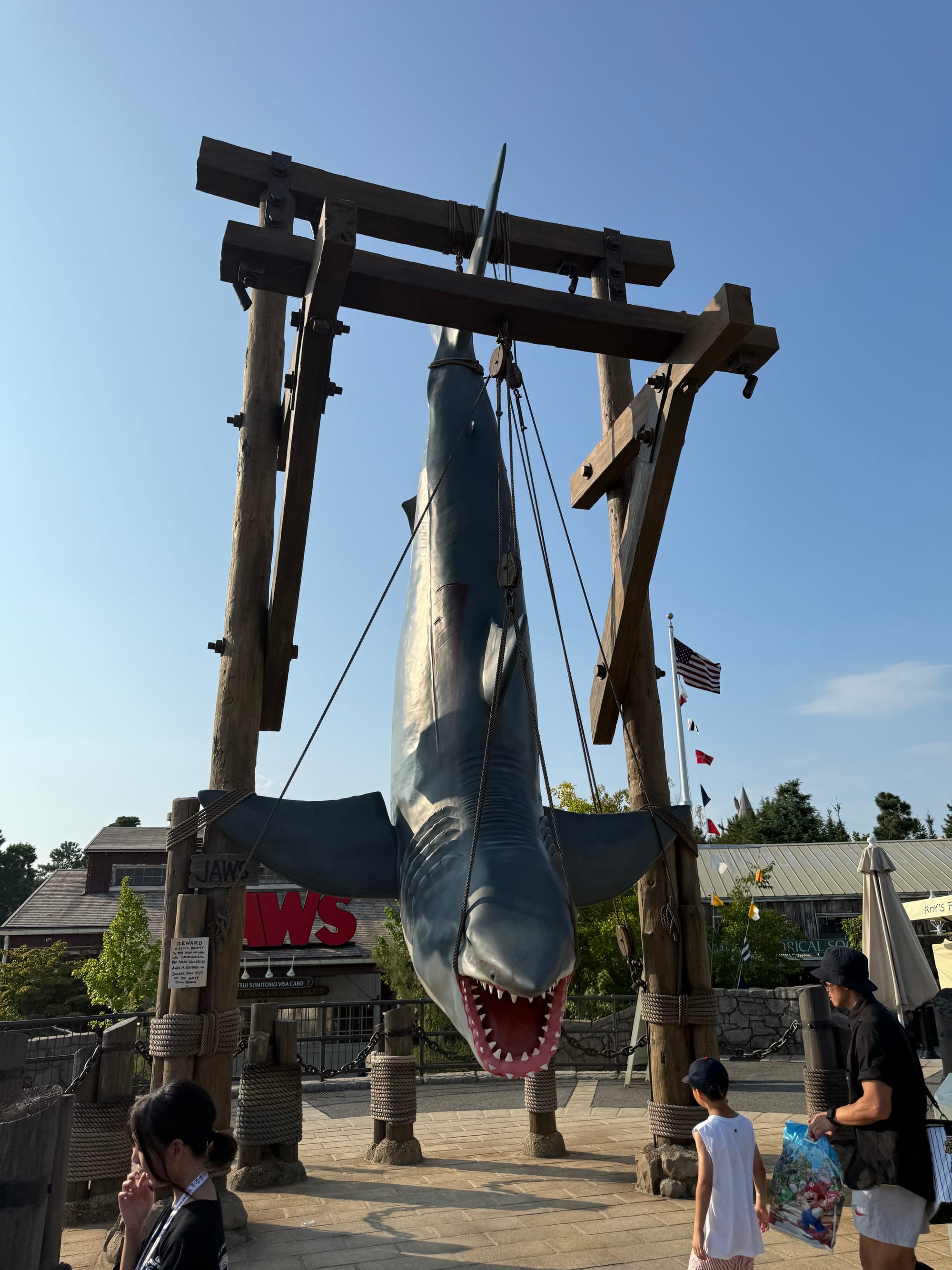 Suspended shark model from Jaws displayed in the Amity area at Universal Studios Japan, hanging from a wooden frame with its mouth open above visitors below.