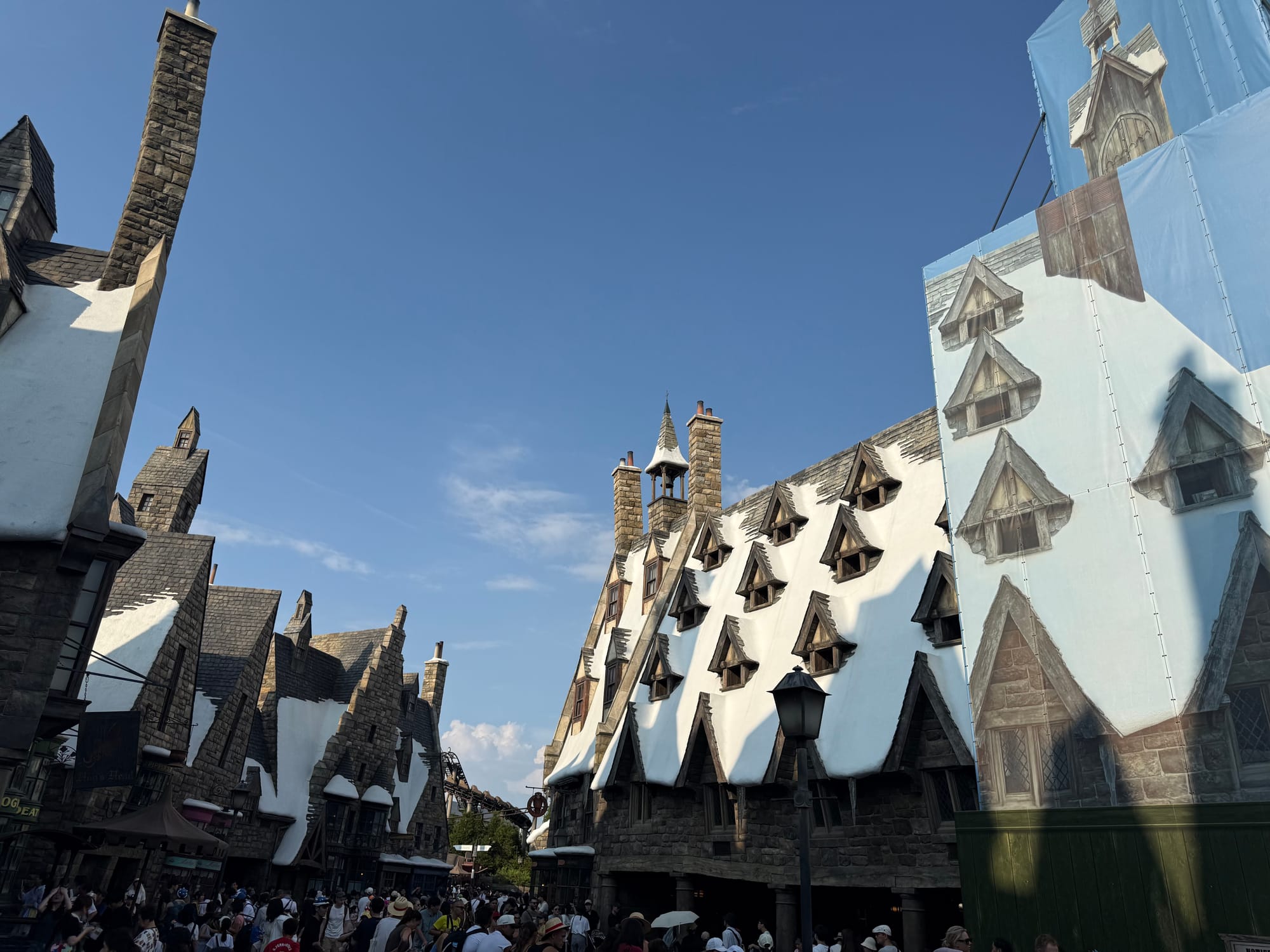 Hogsmeade village in The Wizarding World of Harry Potter at Universal Studios Japan, featuring snow-covered rooftops, stone buildings and crowds along the themed street.