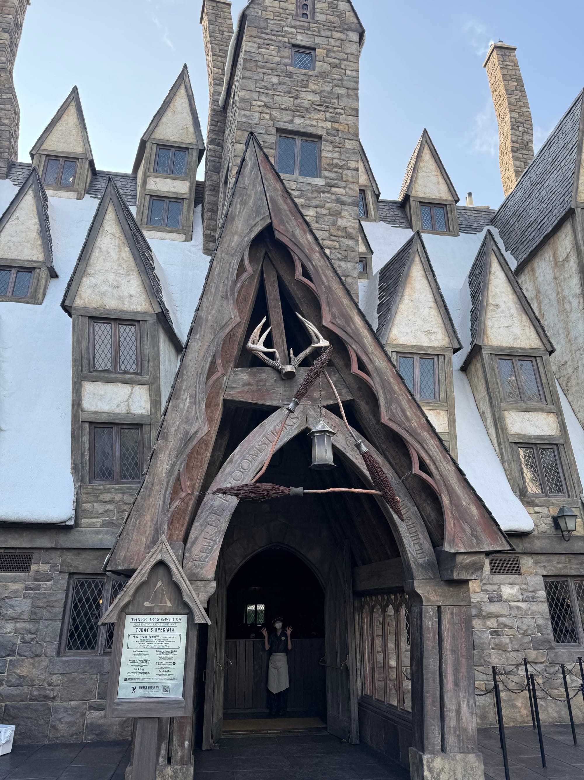 Entrance to the Three Broomsticks in The Wizarding World of Harry Potter at Universal Studios Japan, featuring a steep timber-framed roof, crossed broomsticks and stone-built architecture.
