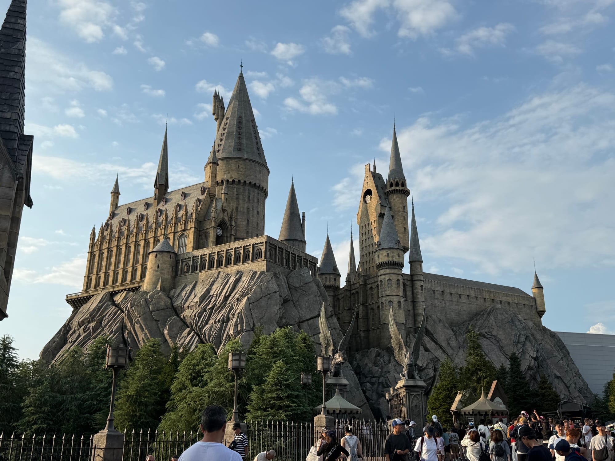 Hogwarts Castle towering above The Wizarding World of Harry Potter at Universal Studios Japan, featuring soaring spires, stone walls and rocky cliffs beneath a blue sky.