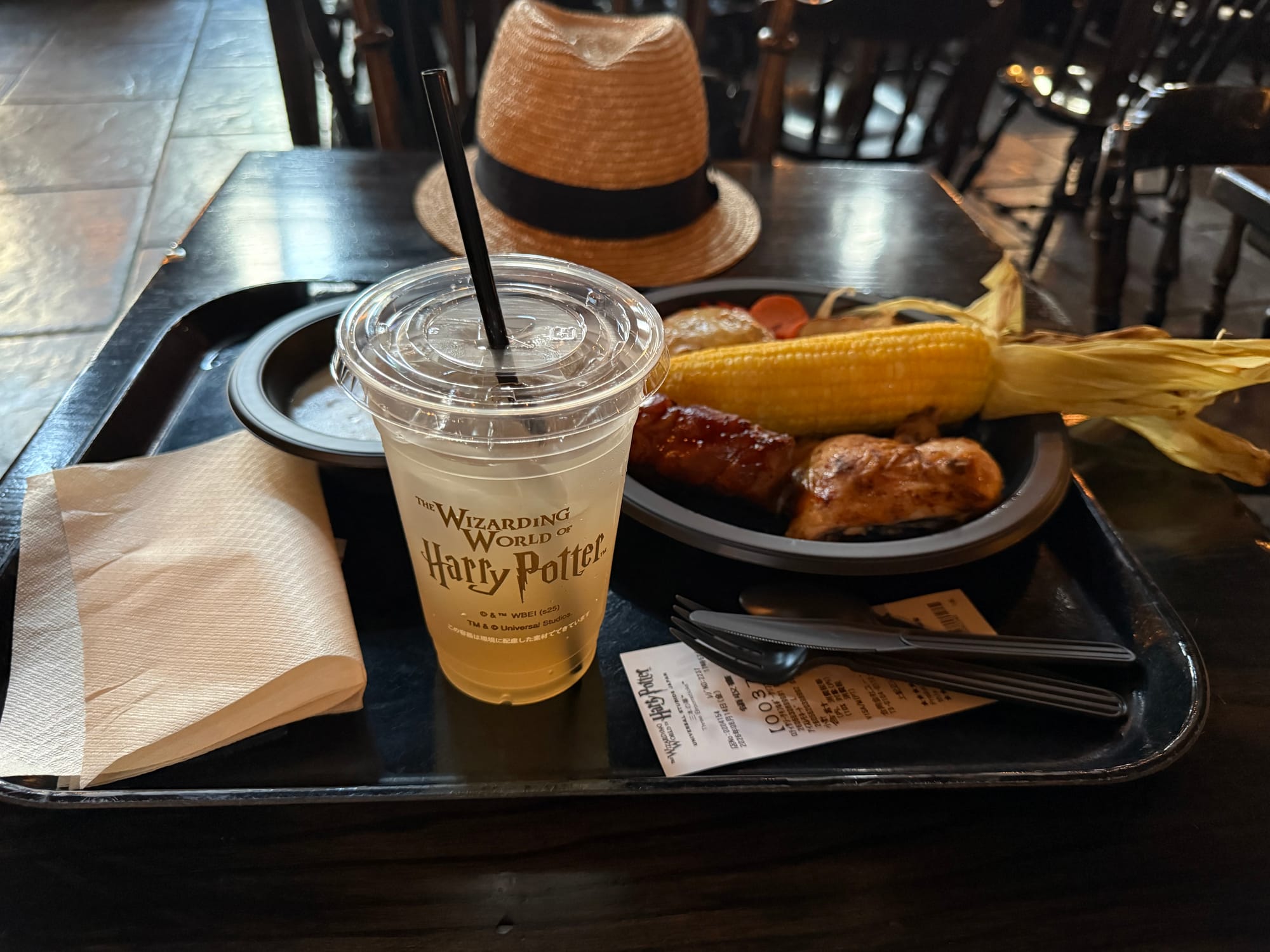 Meal at the Three Broomsticks in The Wizarding World of Harry Potter, featuring roasted chicken, corn on the cob, potatoes and a cup of lemonade on a restaurant tray.