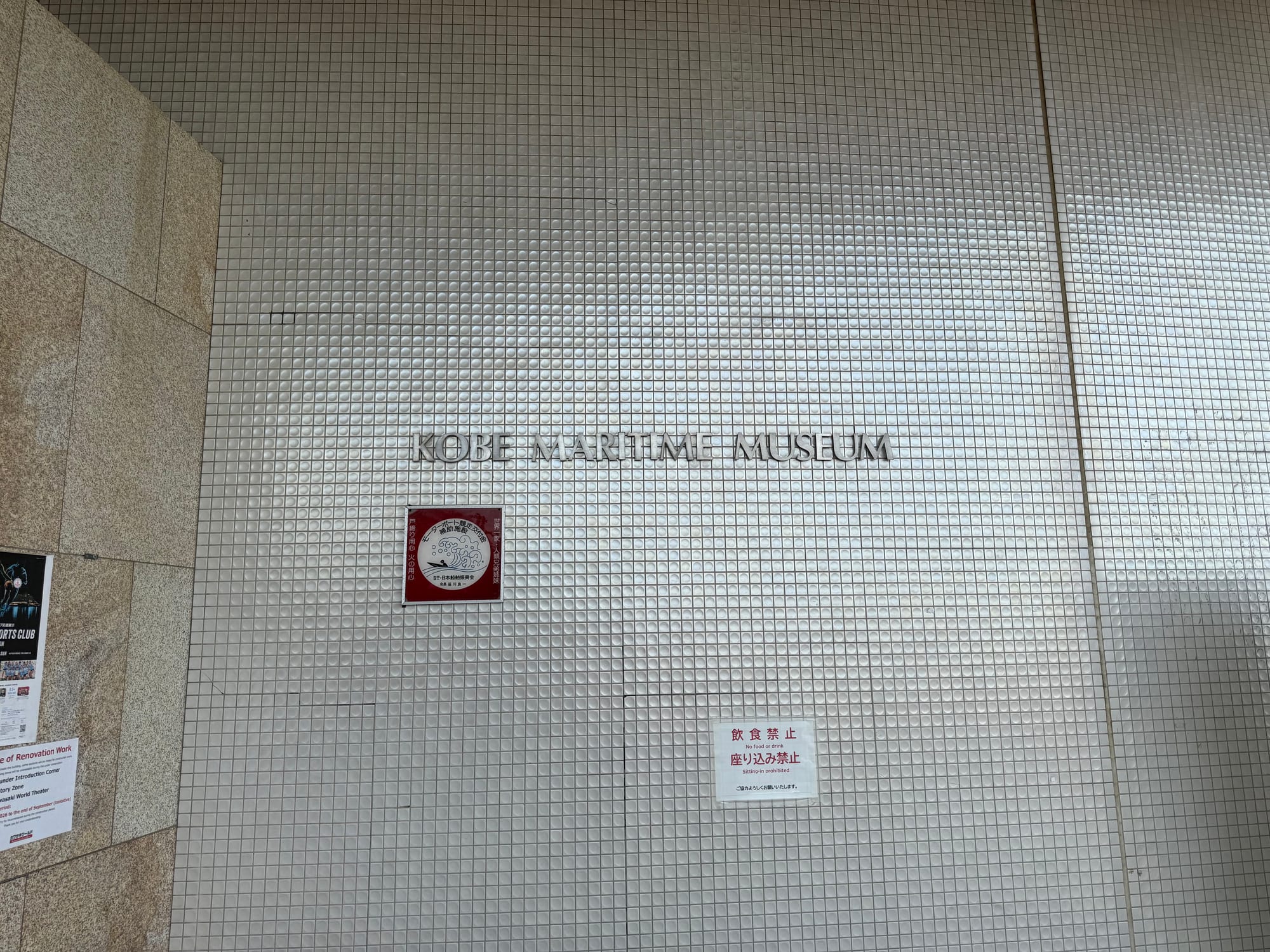 Wall sign for the Kobe Maritime Museum, displaying the museum name in metallic lettering against a textured tiled surface near the entrance to the waterfront attraction.