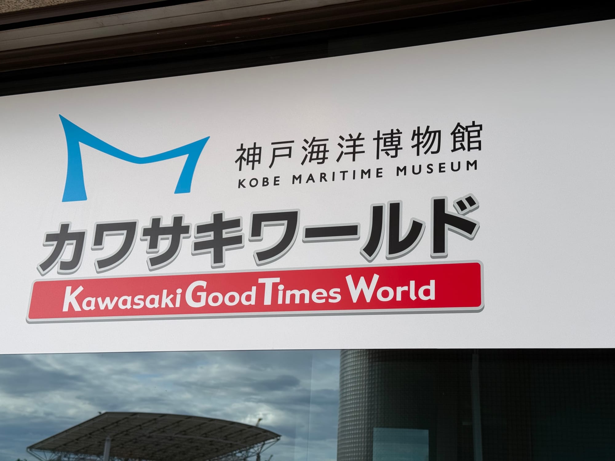 Sign for Kawasaki Good Times World inside the Kobe Maritime Museum, featuring the exhibition logo and bilingual Japanese and English text at the entrance to the Kawasaki-themed gallery.