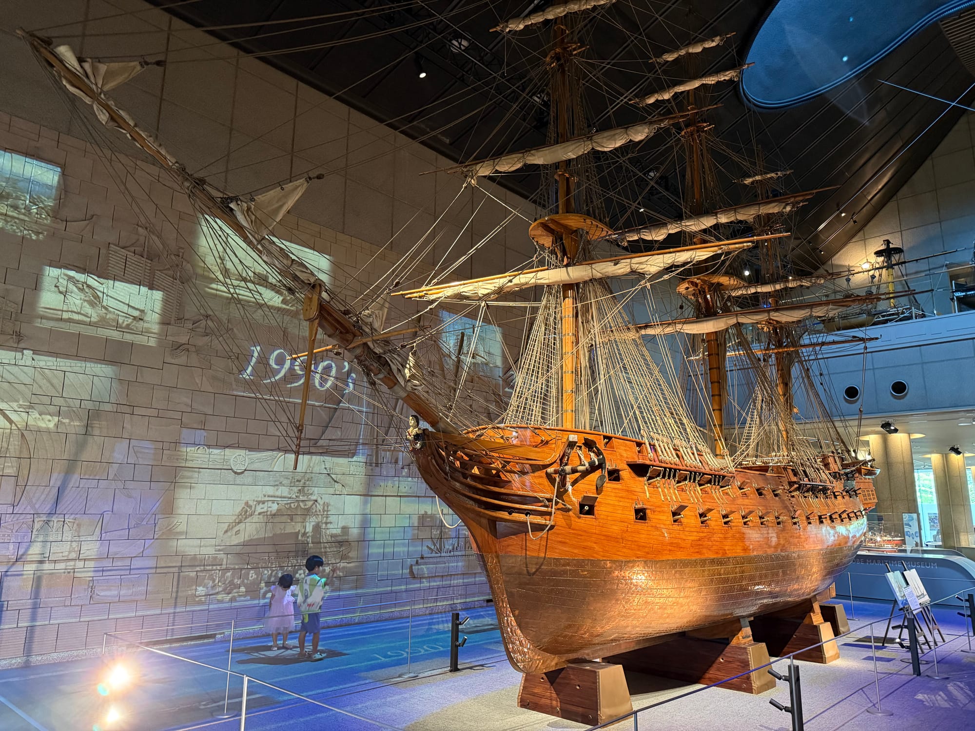 Scale model of an early European-style sailing ship displayed at the Kobe Maritime Museum, featuring detailed masts, rigging, gun ports and wooden hull construction.