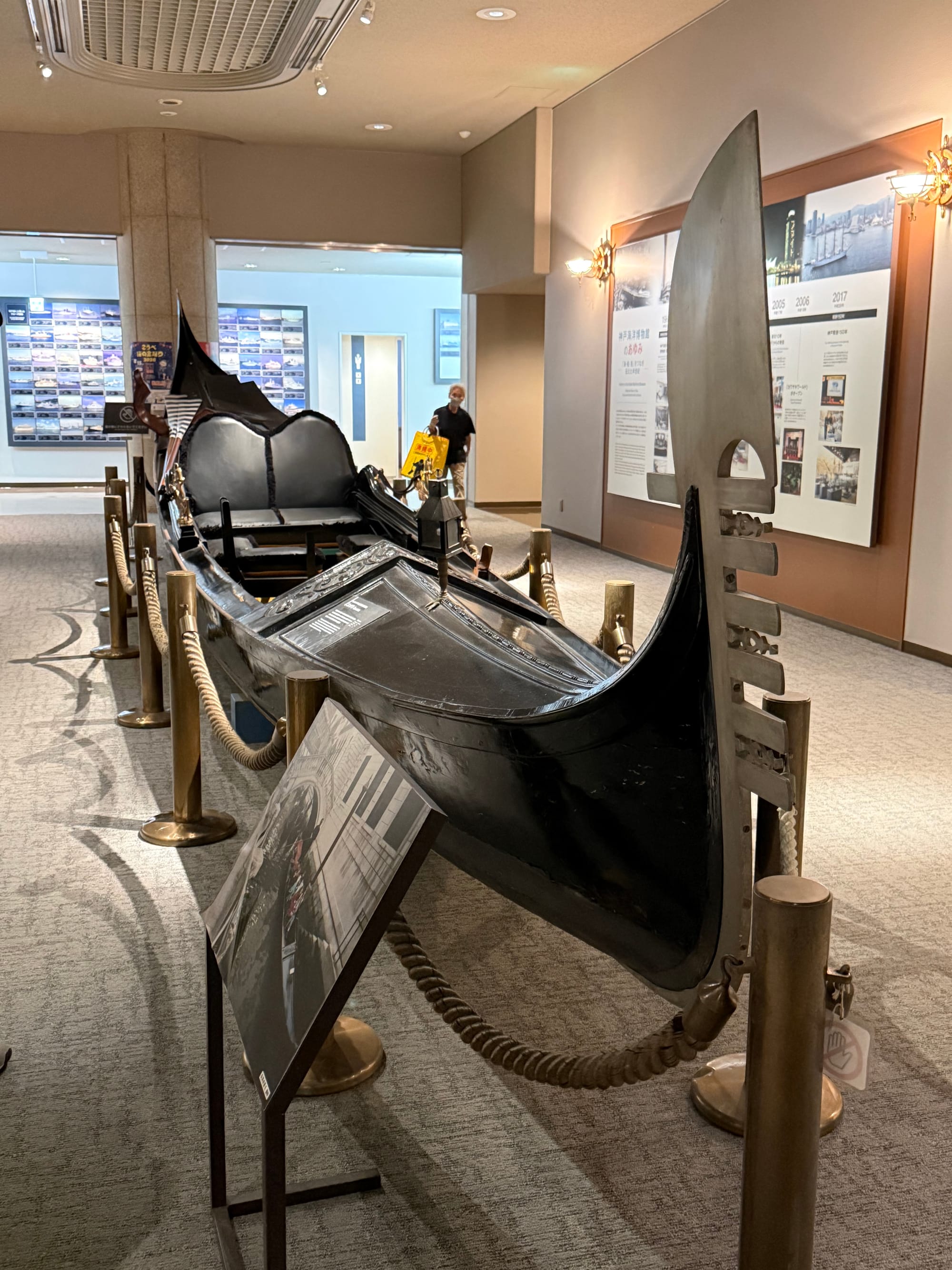 Traditional Venetian gondola displayed at the Kobe Maritime Museum, featuring a black lacquered hull, ornate details, passenger seating and the distinctive curved iron prow.