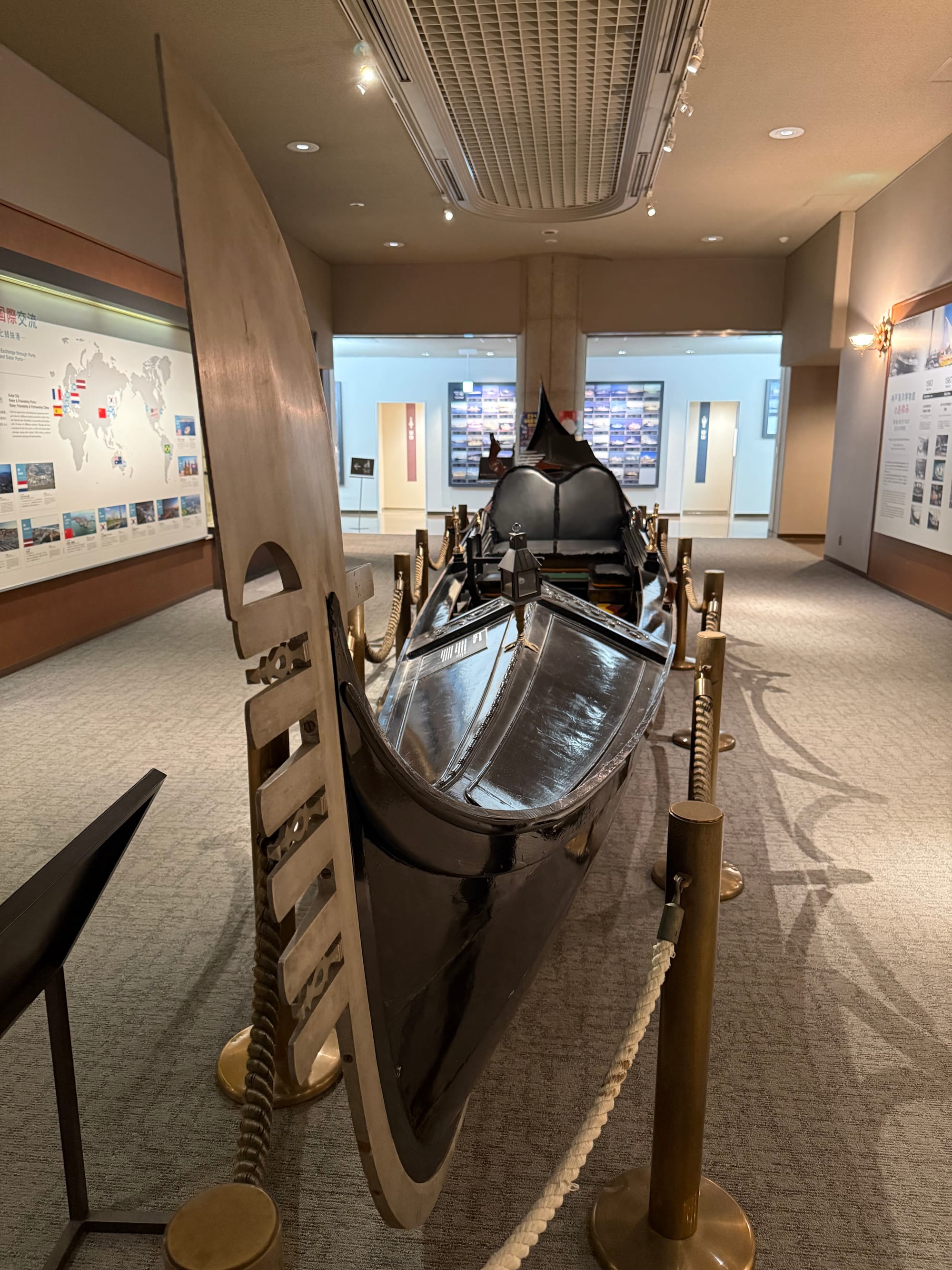 Traditional Venetian gondola displayed at the Kobe Maritime Museum, viewed from the prow, highlighting the distinctive iron ferro, black hull and elegant asymmetrical design.