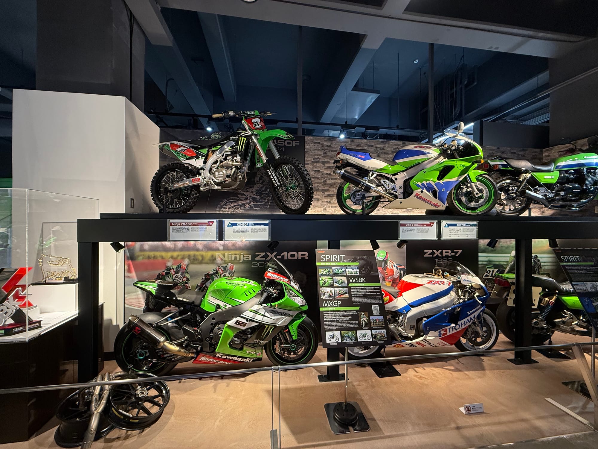 Collection of Kawasaki motorcycles displayed at Kawasaki Good Times World in Kobe, including Ninja ZX-10R, ZXR-7, KX450F motocross and classic road bikes highlighting racing heritage.
