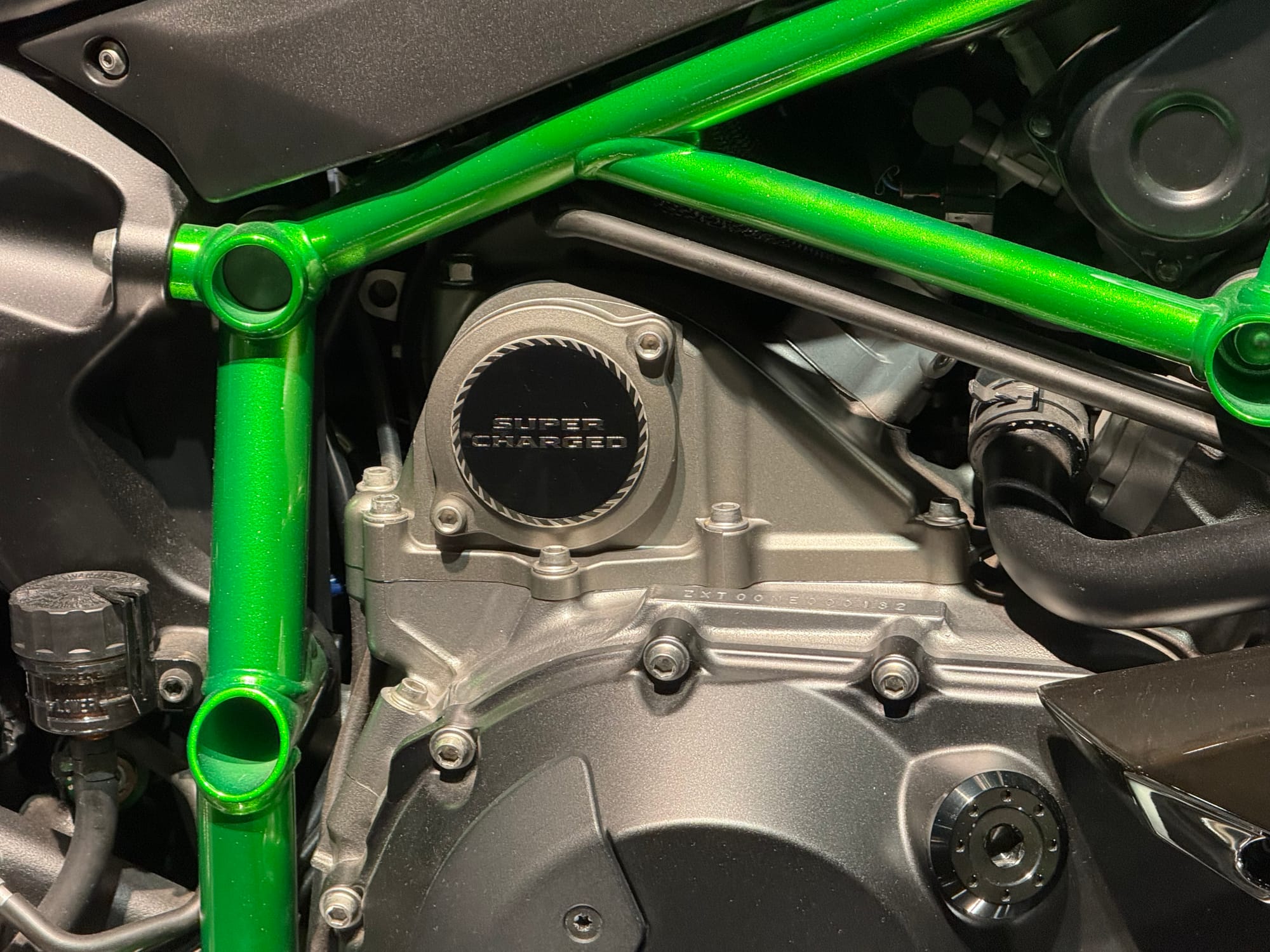 Close-up of the supercharged engine on a Kawasaki Ninja H2, showing the green trellis frame, engine casing and "SUPER CHARGED" badge at Kawasaki Good Times World.
